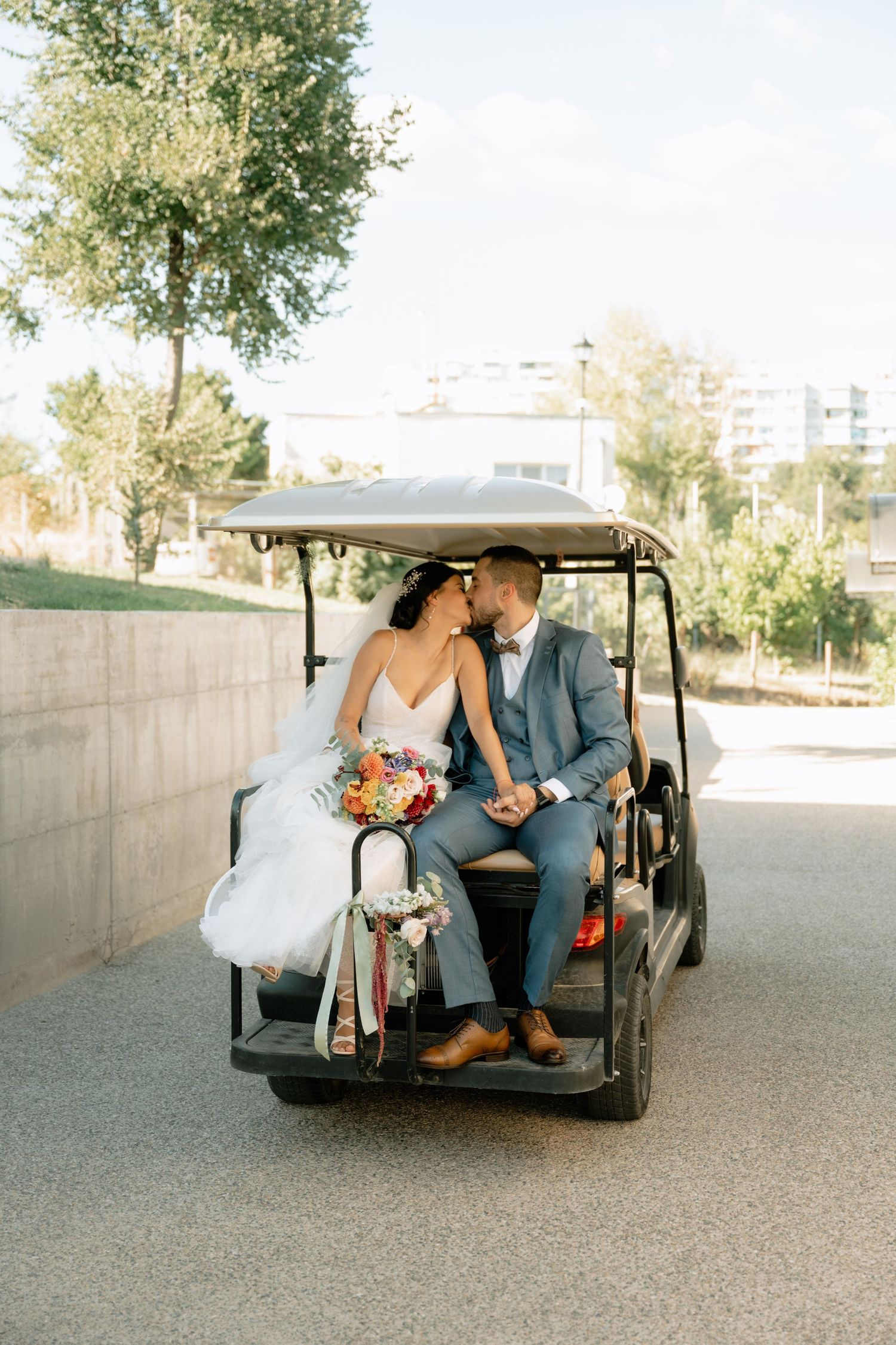 A romantic couple sits together in a golf cart during a wedding photoshoot in an urban setting.