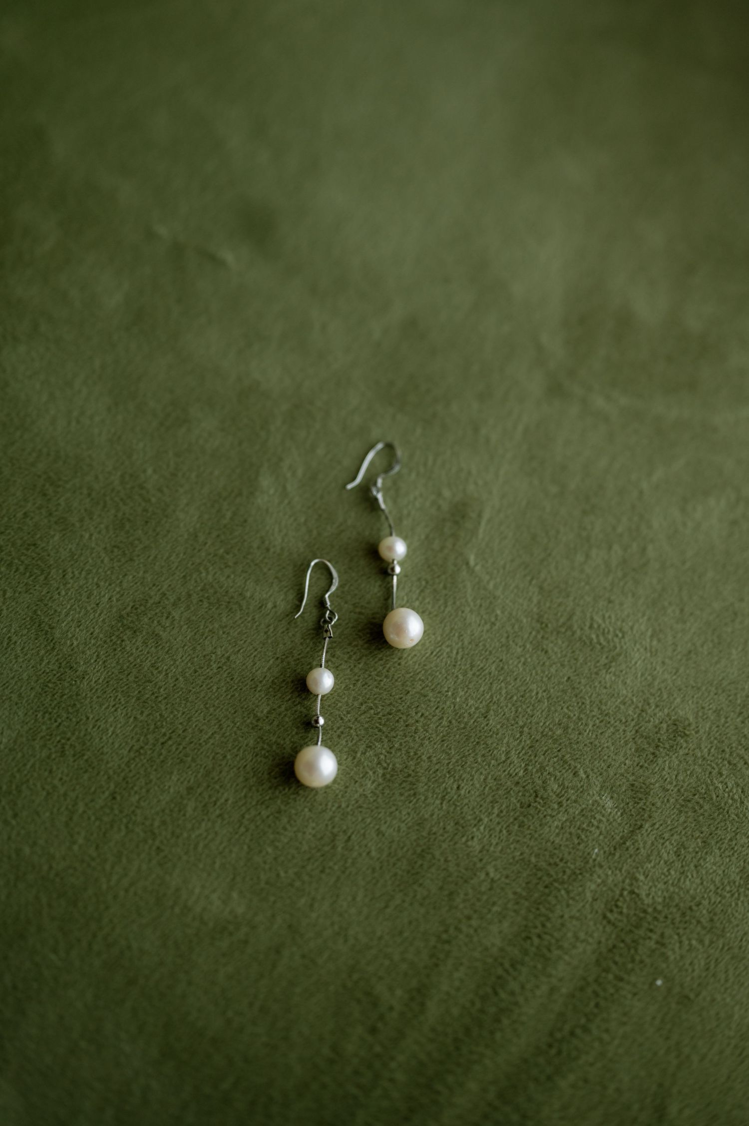 Pearl drop earrings displayed on a green velvet background in various angles.