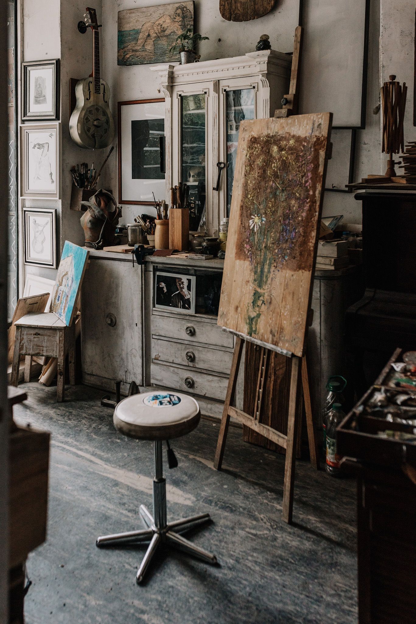 Vintage art studio interior with wooden easels and antique furniture against white walls.