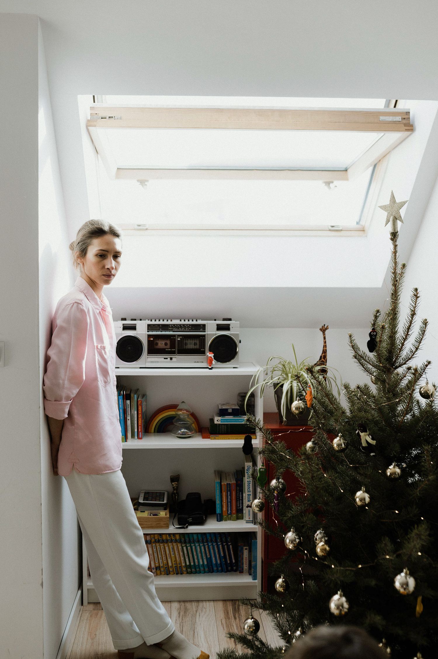 A sequence showing someone in a pink sweater and white pants dancing next to a decorated Christmas tree and vintage boombox.