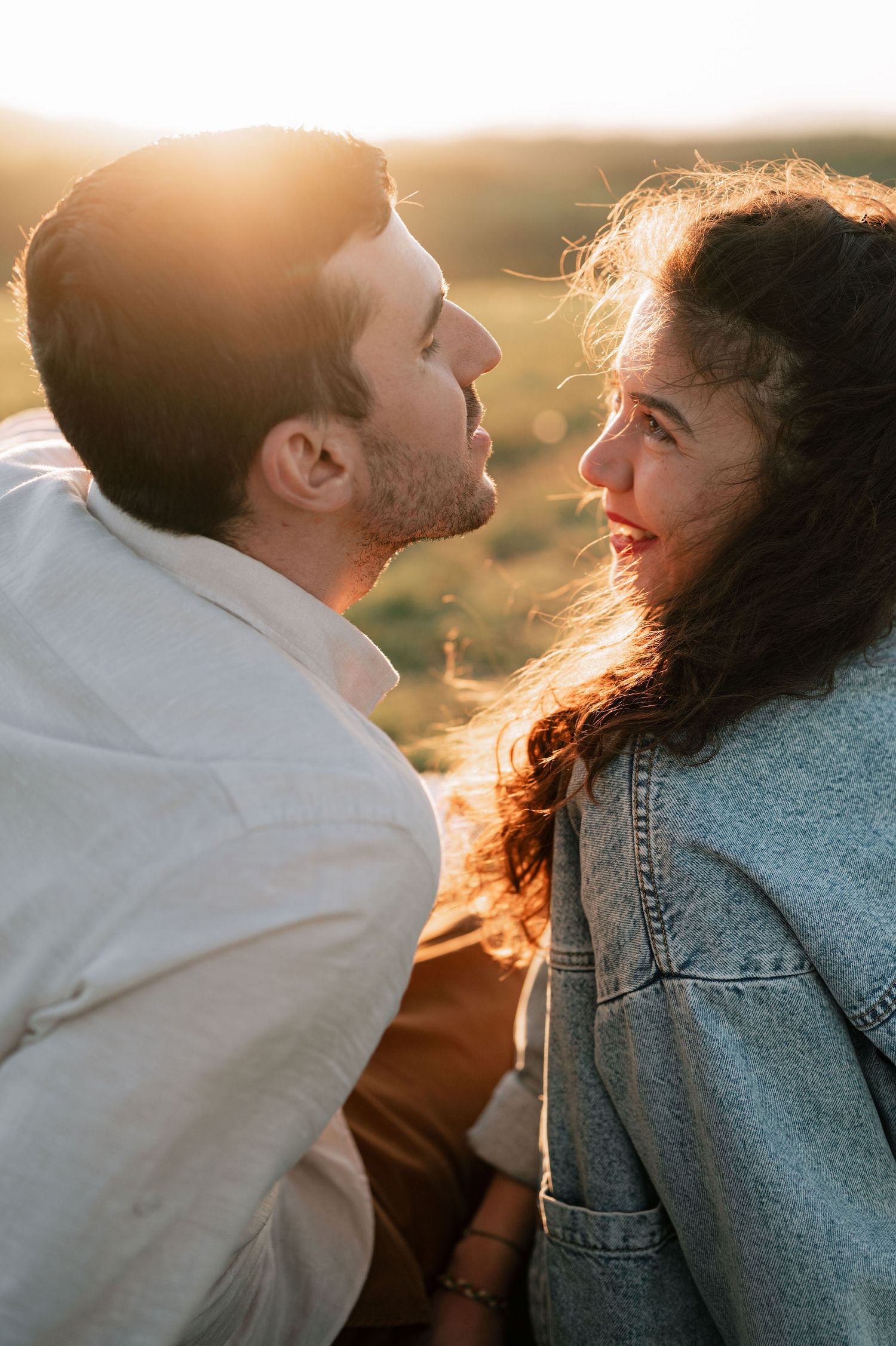 A couple in casual attire shares a tender moment at sunset with golden light illuminating their silhouettes.