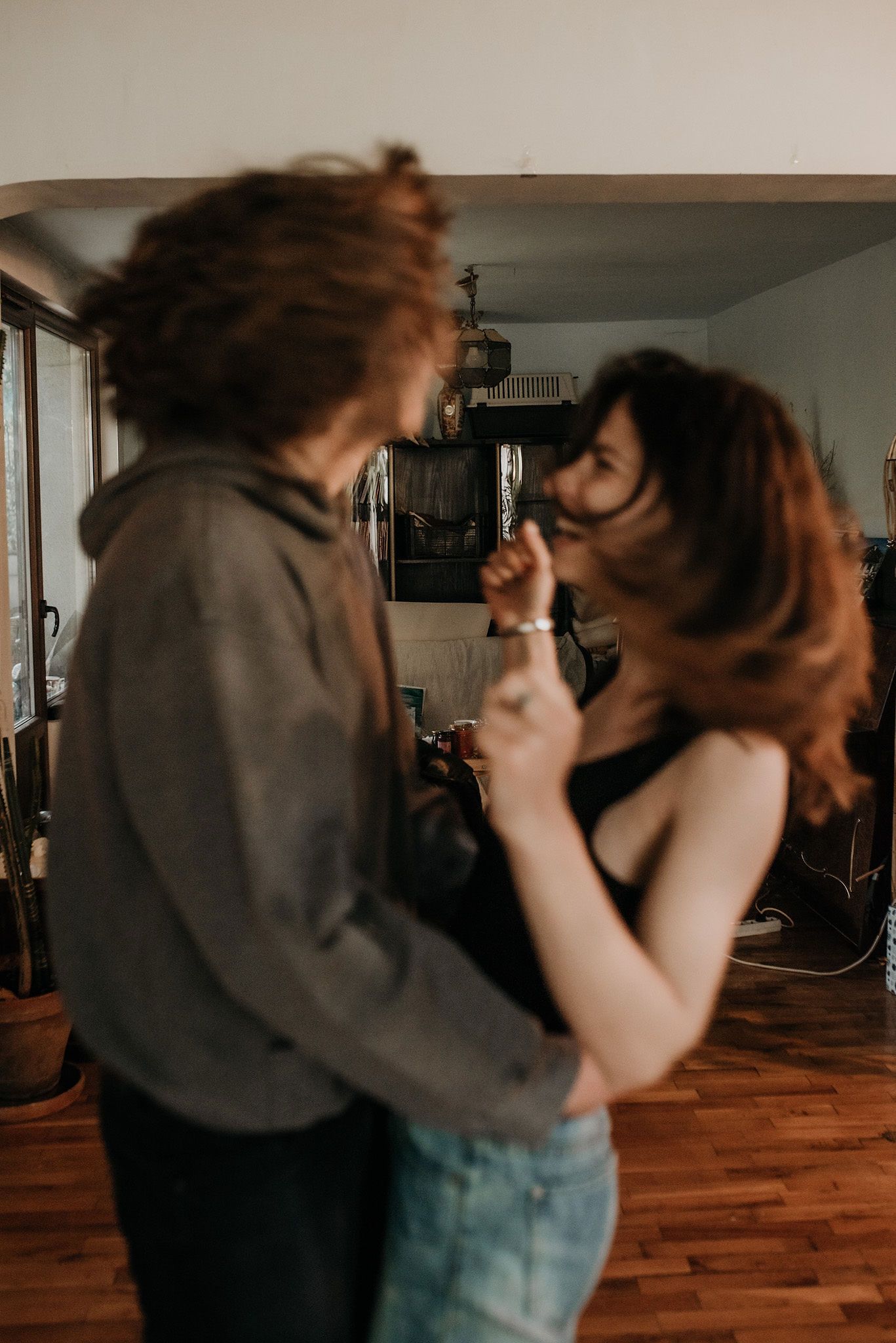 Two people in casual attire dance together in a room with wooden floors in a sequence of intimate dance moves.