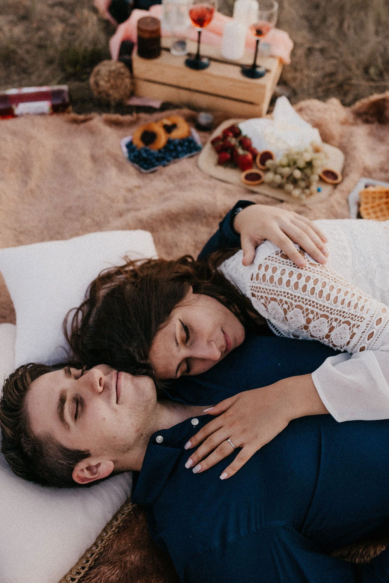 Couple lying together on white surface with gentle expressions and casual attire.