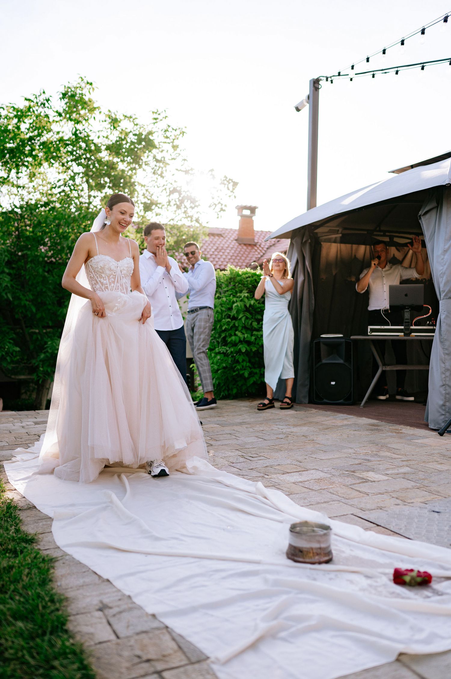 Wedding celebration participants stand around white cloth on stone patio.