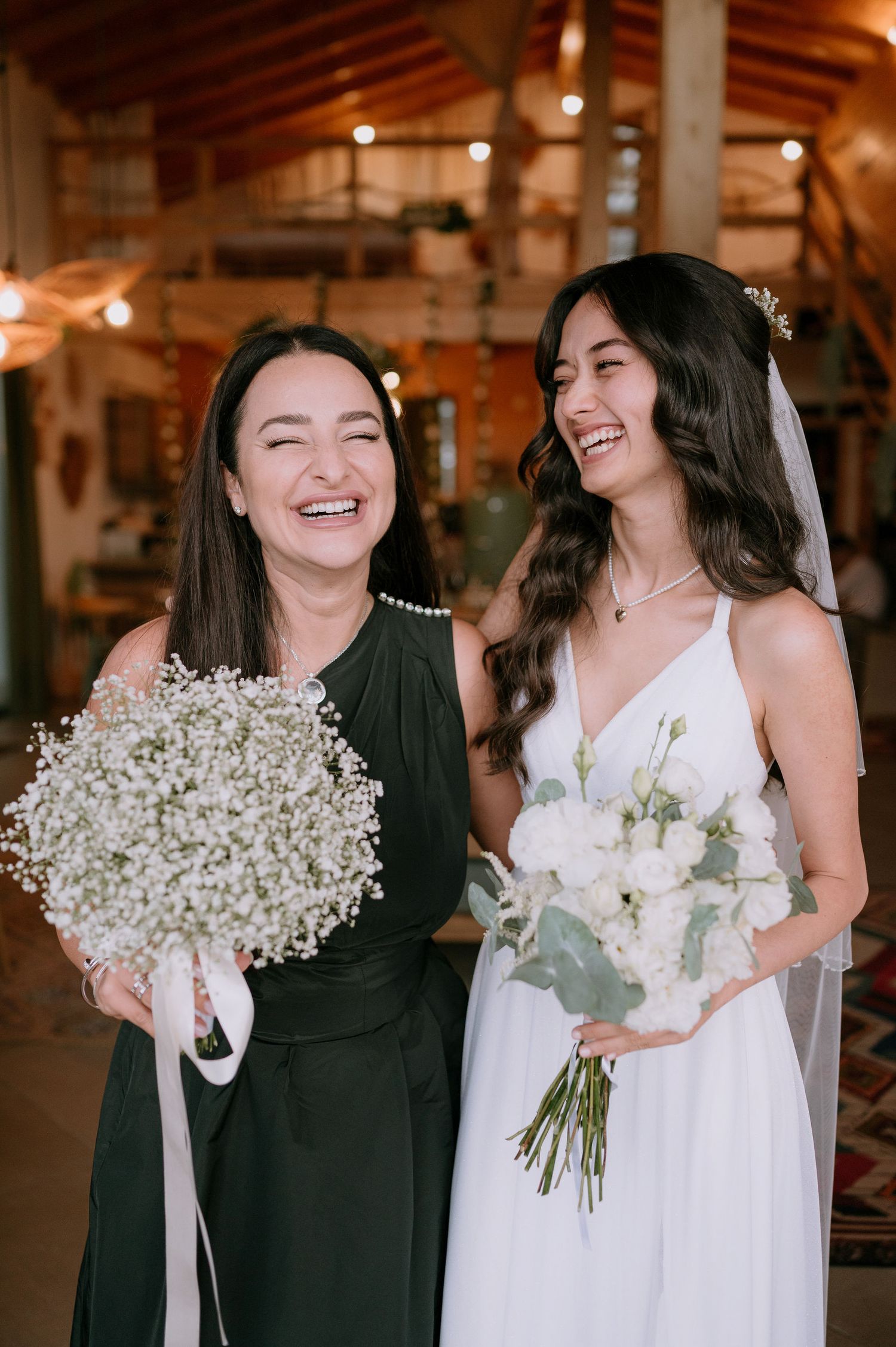 Wedding party members in black and white dresses holding baby's breath bouquets while laughing together.