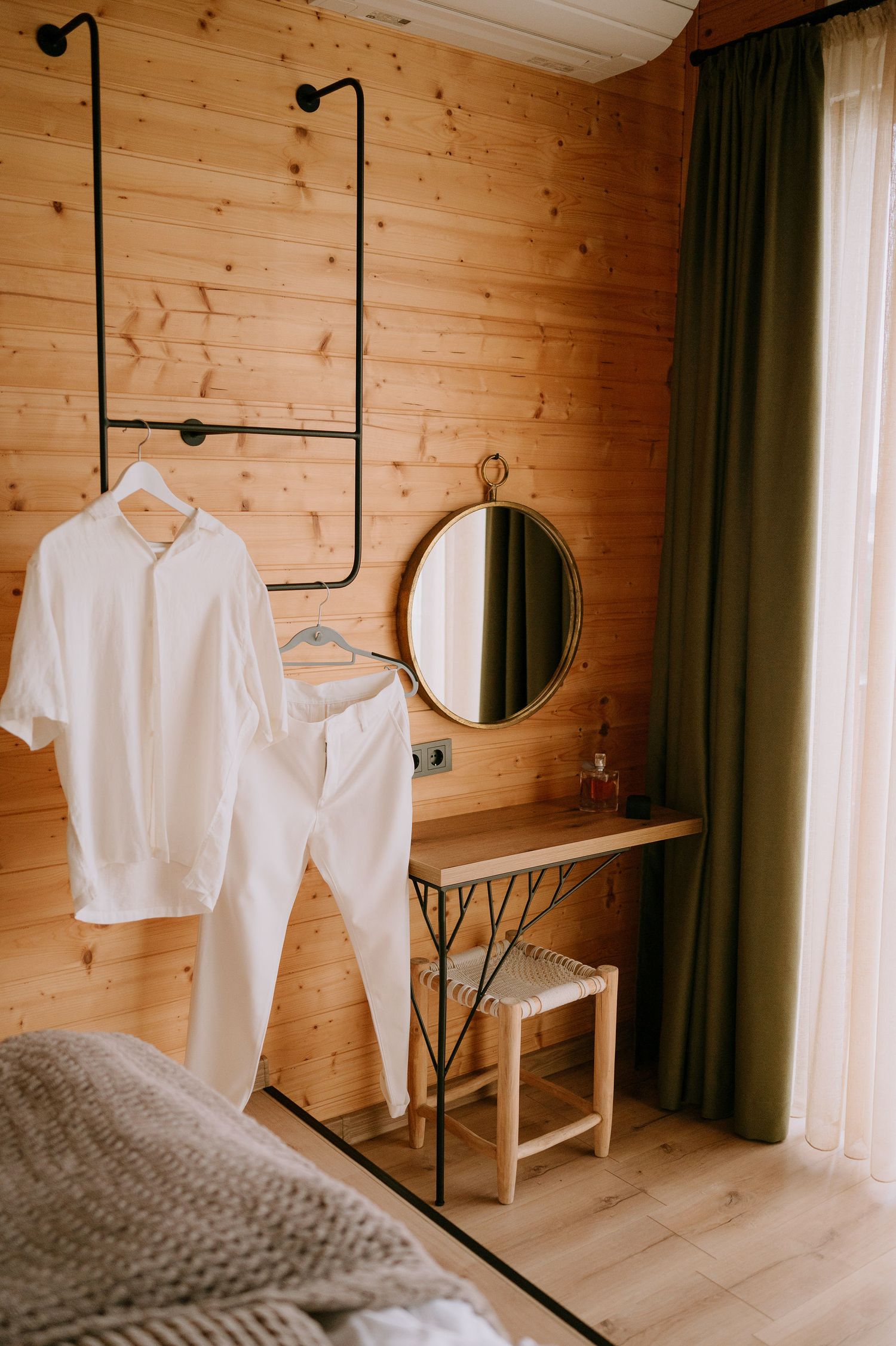 White clothing hangs on industrial pipe rack against wooden wall with round mirror.