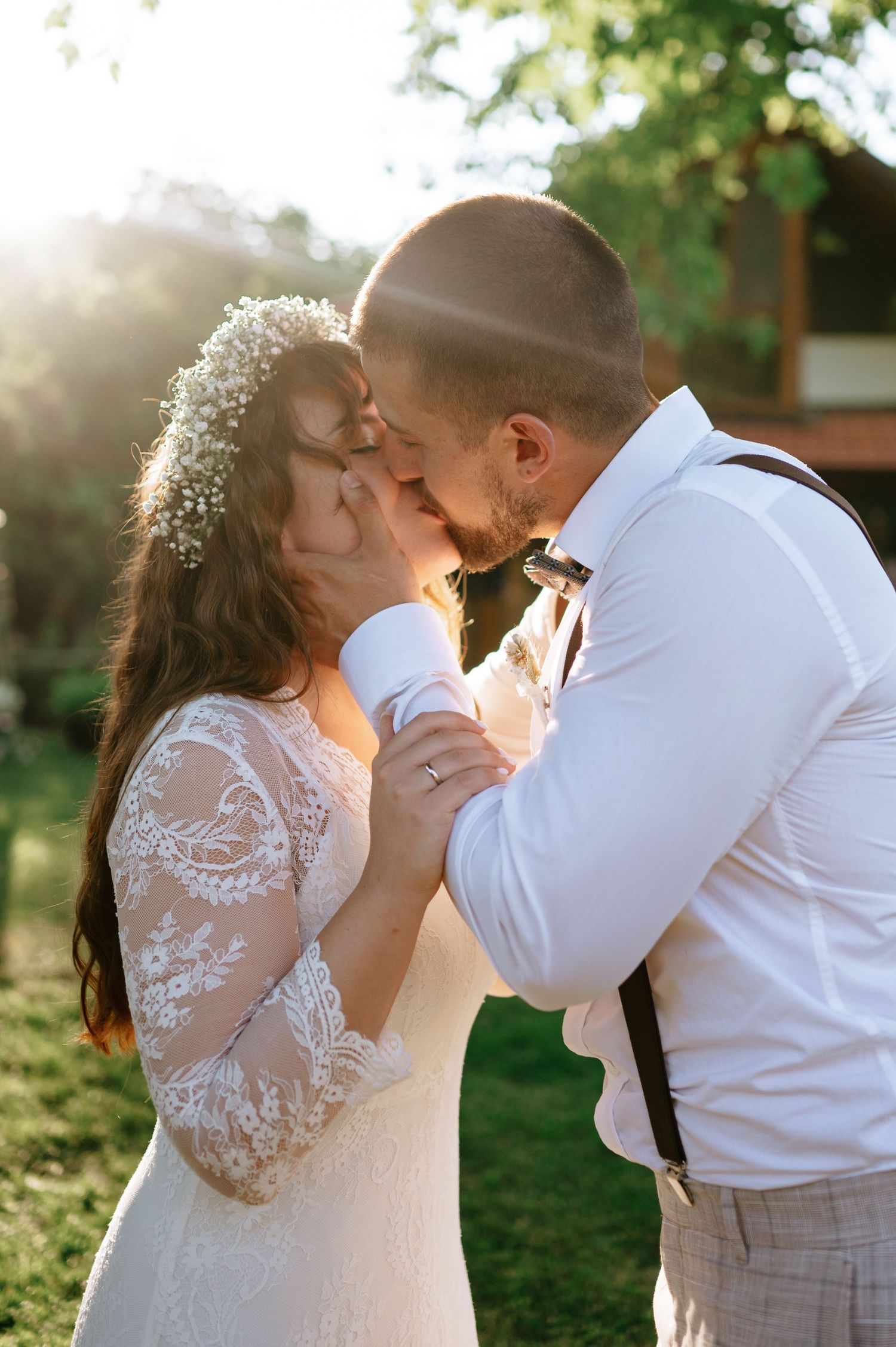 Couple sharing their first kiss as newlyweds under a sunlit garden backdrop.