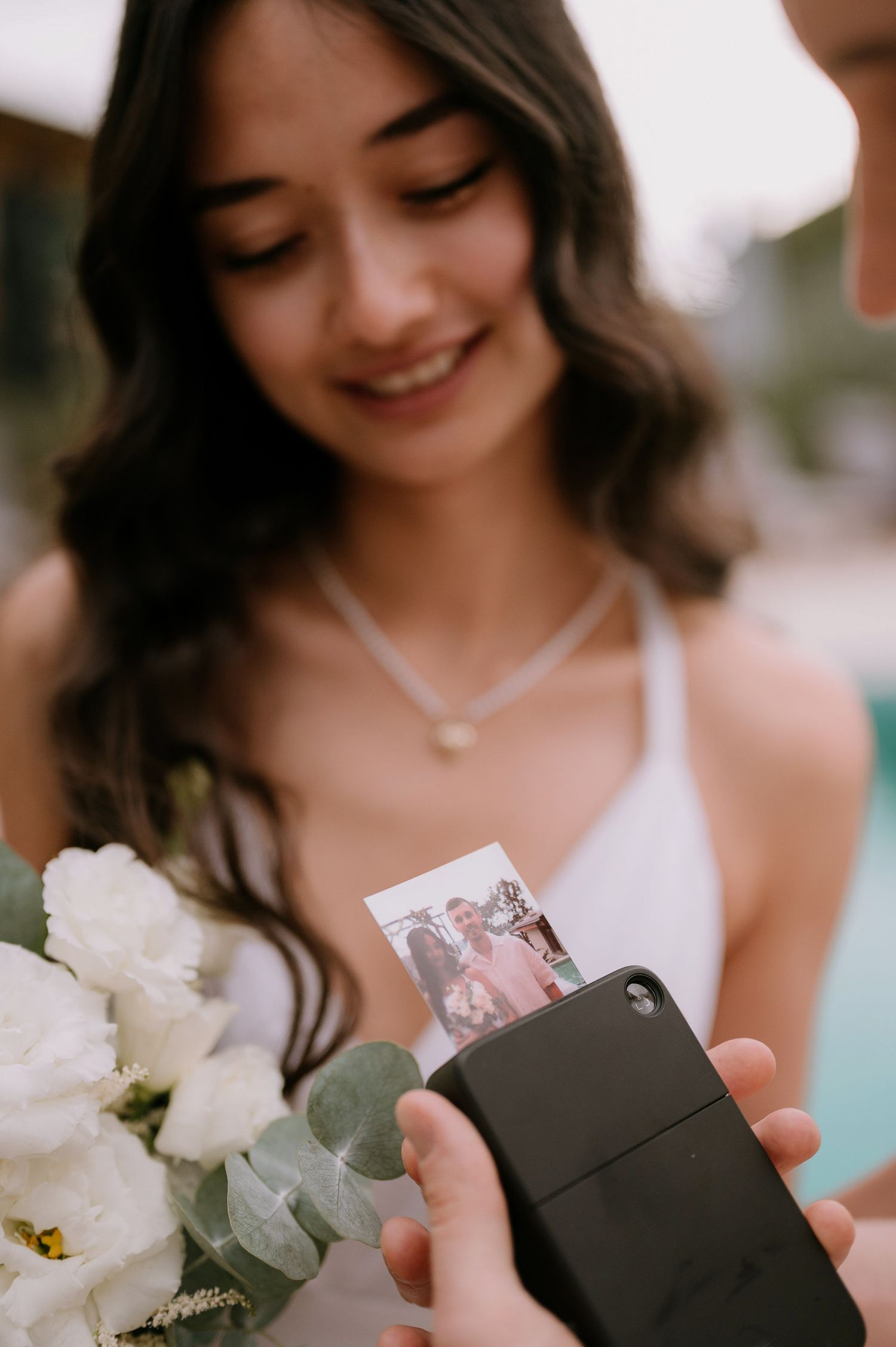 A person in white holding a small black box and bouquet against a blurred background.