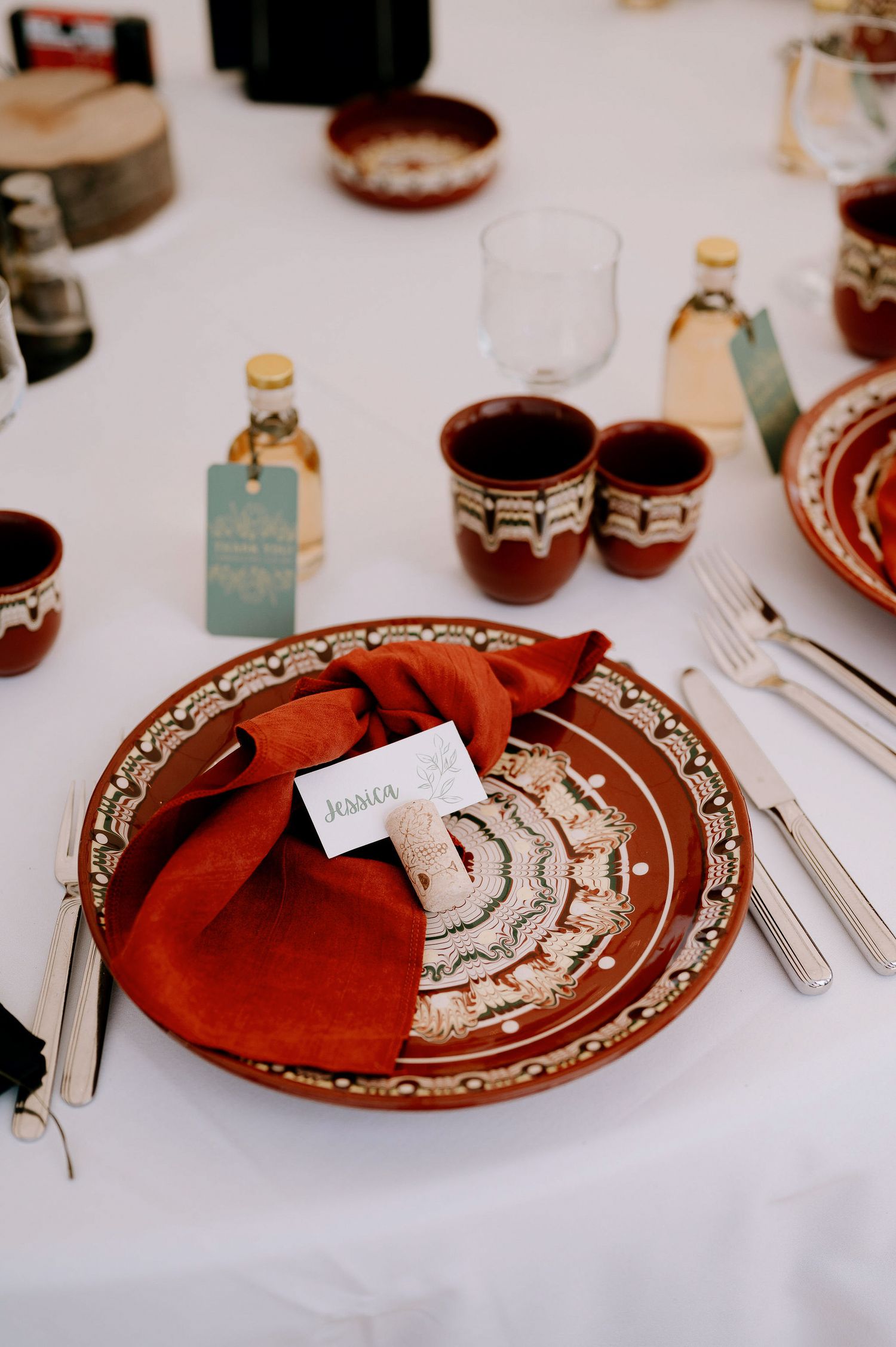 Elegant table settings with rustic red plates and napkins on white tablecloths at a formal event.