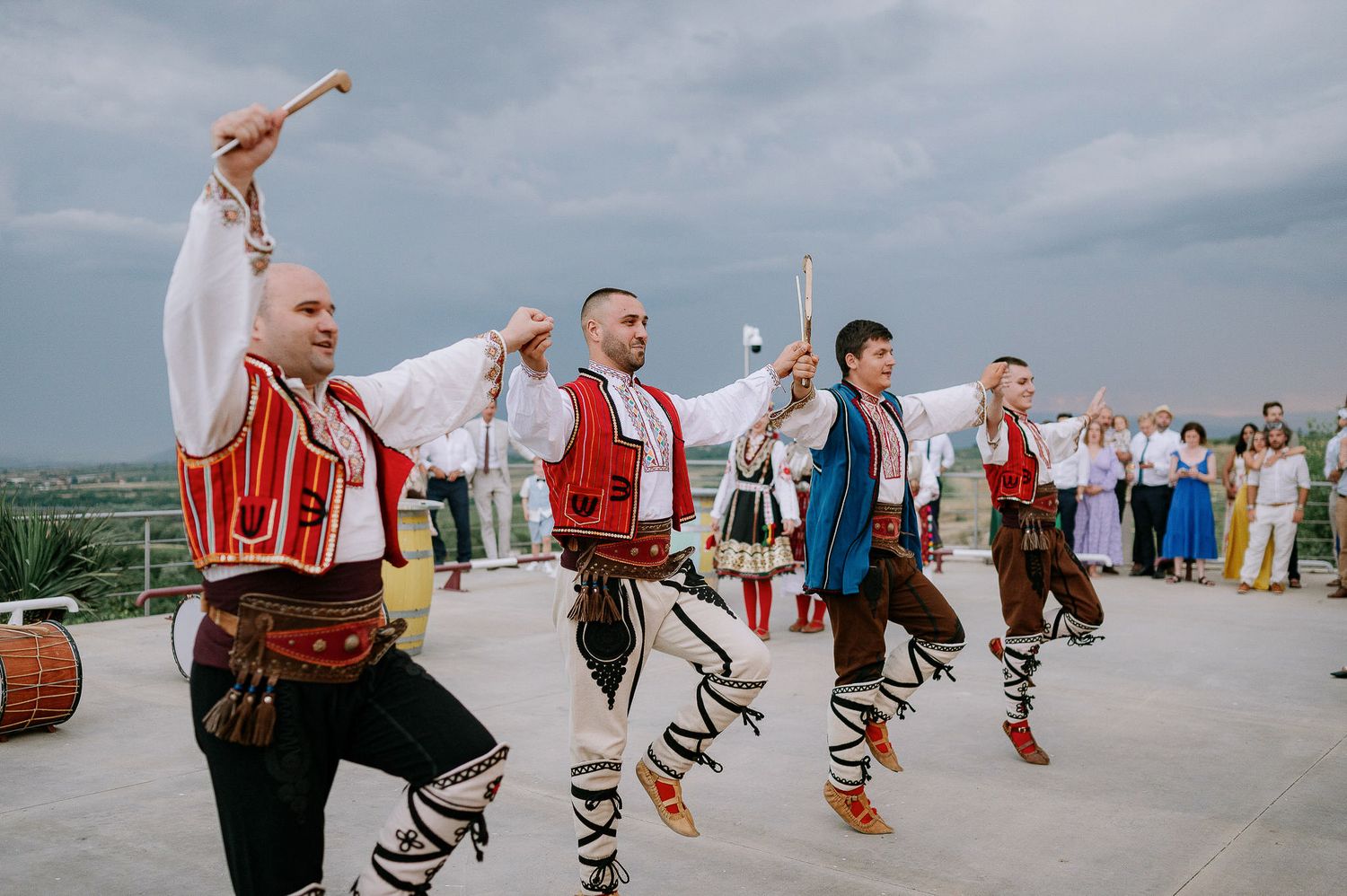 Traditional folk dancers perform in colorful costumes against a cloudy sky.