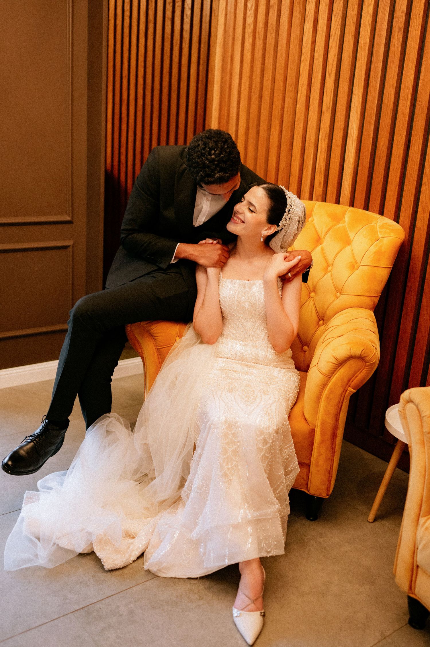 Romantic wedding portrait session with yellow velvet chair and wood-paneled backdrop.