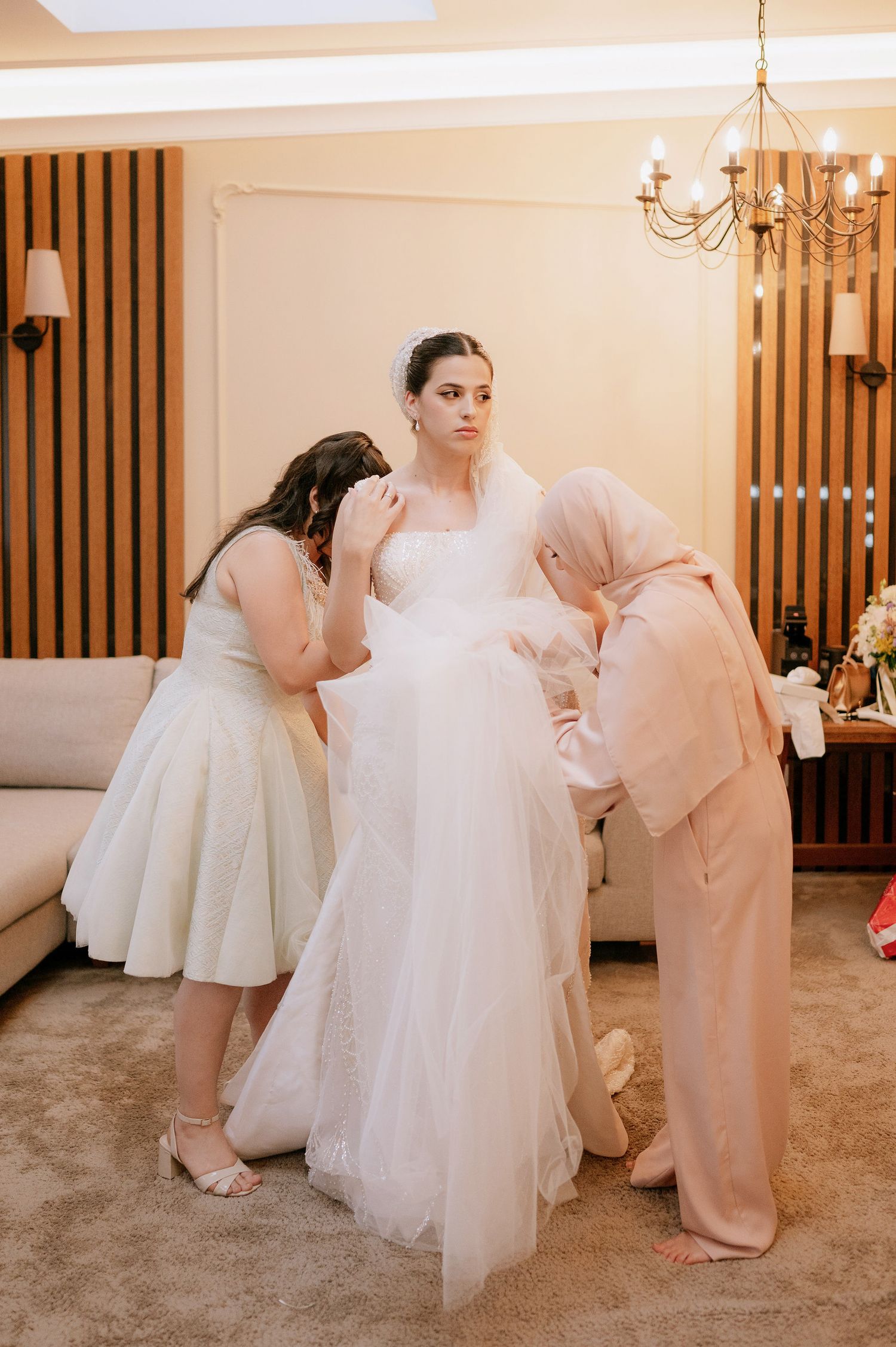 Candid moments of wedding dress preparation with attendants helping arrange the gown's details.