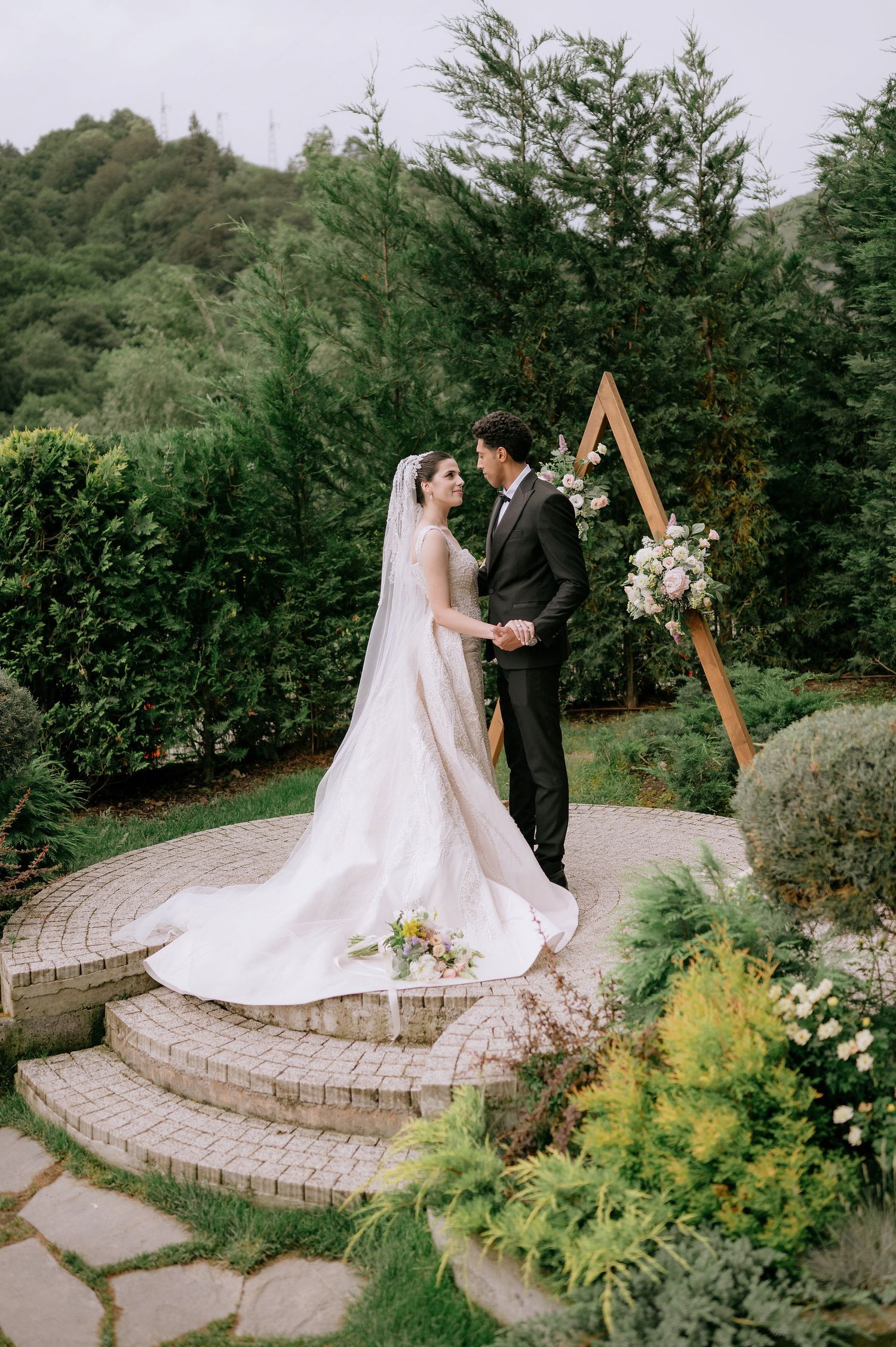 Couple sharing an intimate moment on a curved stone patio with wooden arch and floral arrangements.