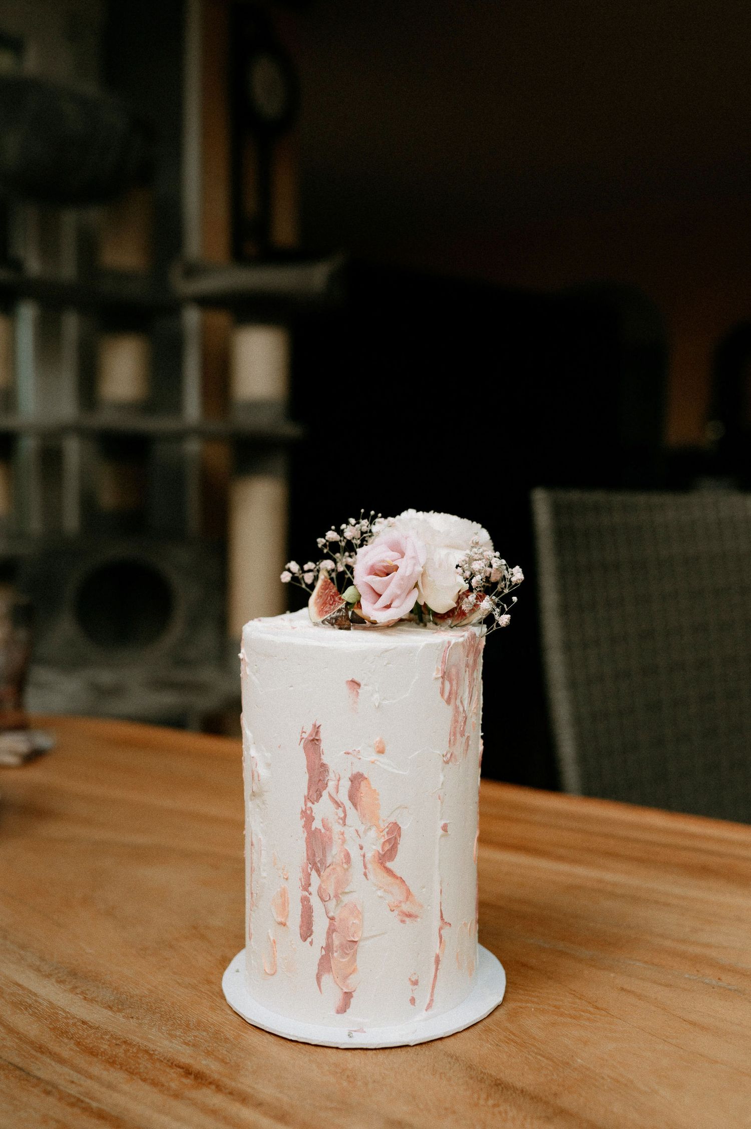 White wedding cake with pink watercolor details and floral decorations displayed on wooden surface.