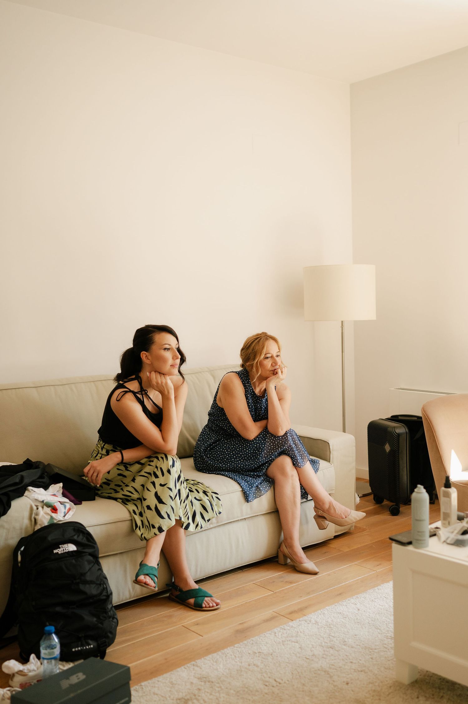 People relaxing on white couch in minimalist room with wooden floors.
