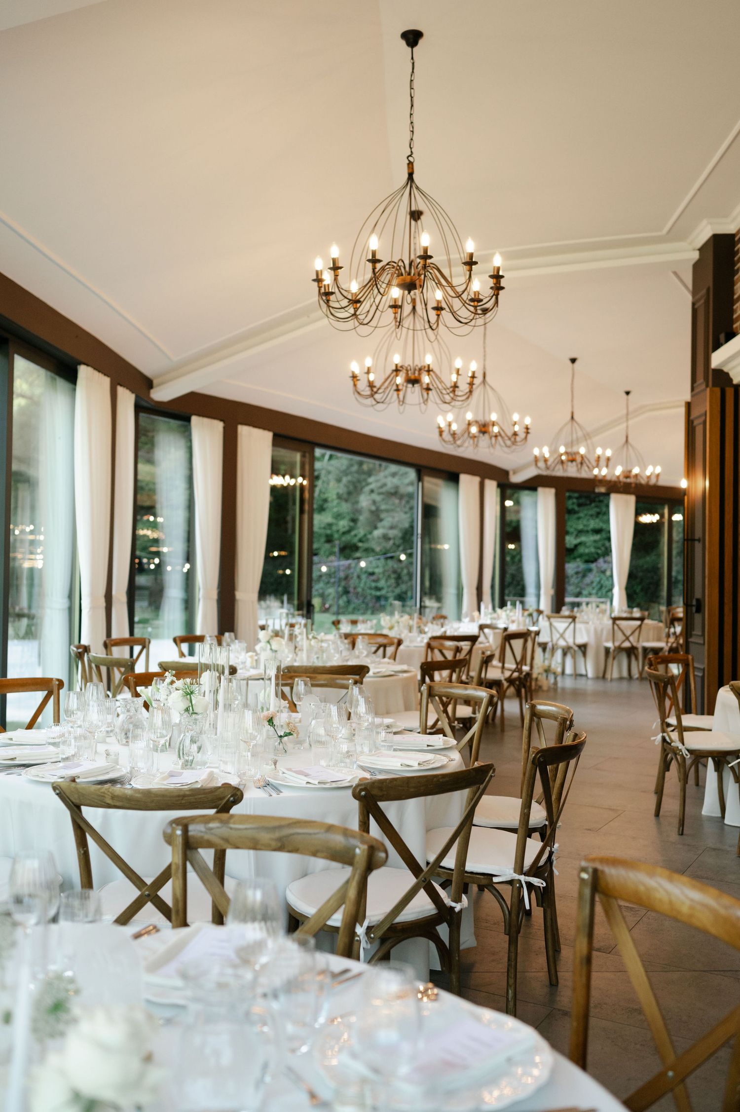Elegant banquet hall with crystal chandeliers and rustic wooden chairs set for formal dining.