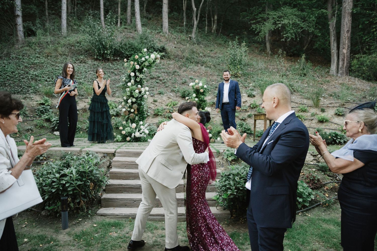 Outdoor celebration with guests mingling in a wooded garden setting.