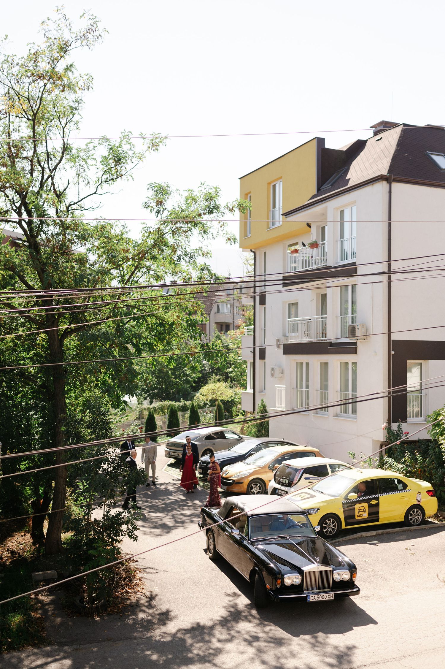 A vintage Rolls Royce parked on a street with apartment buildings and trees.