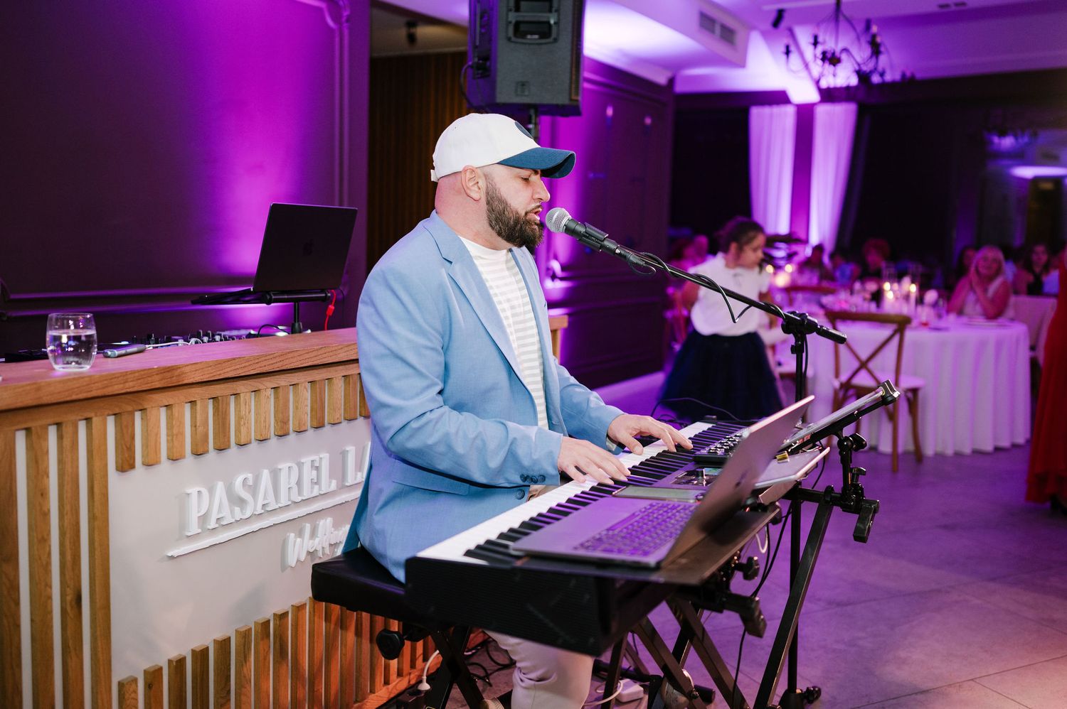 Performer in light blue jacket playing keyboard during wedding reception entertainment.