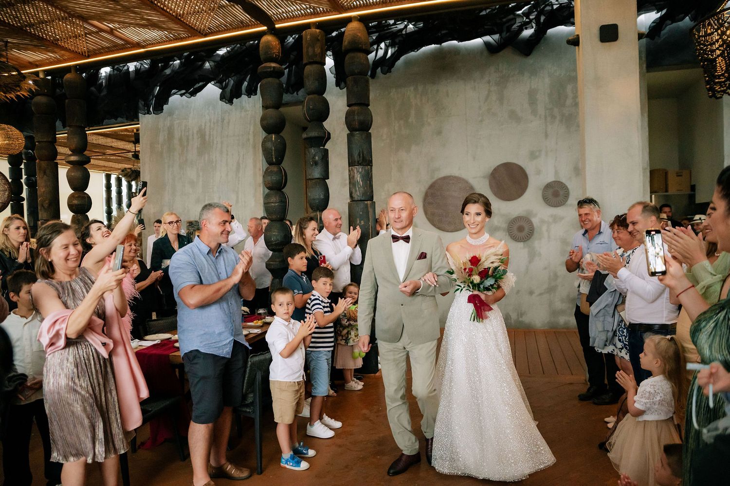 Wedding celebration with guests lined up along both sides of the room clapping and cheering.