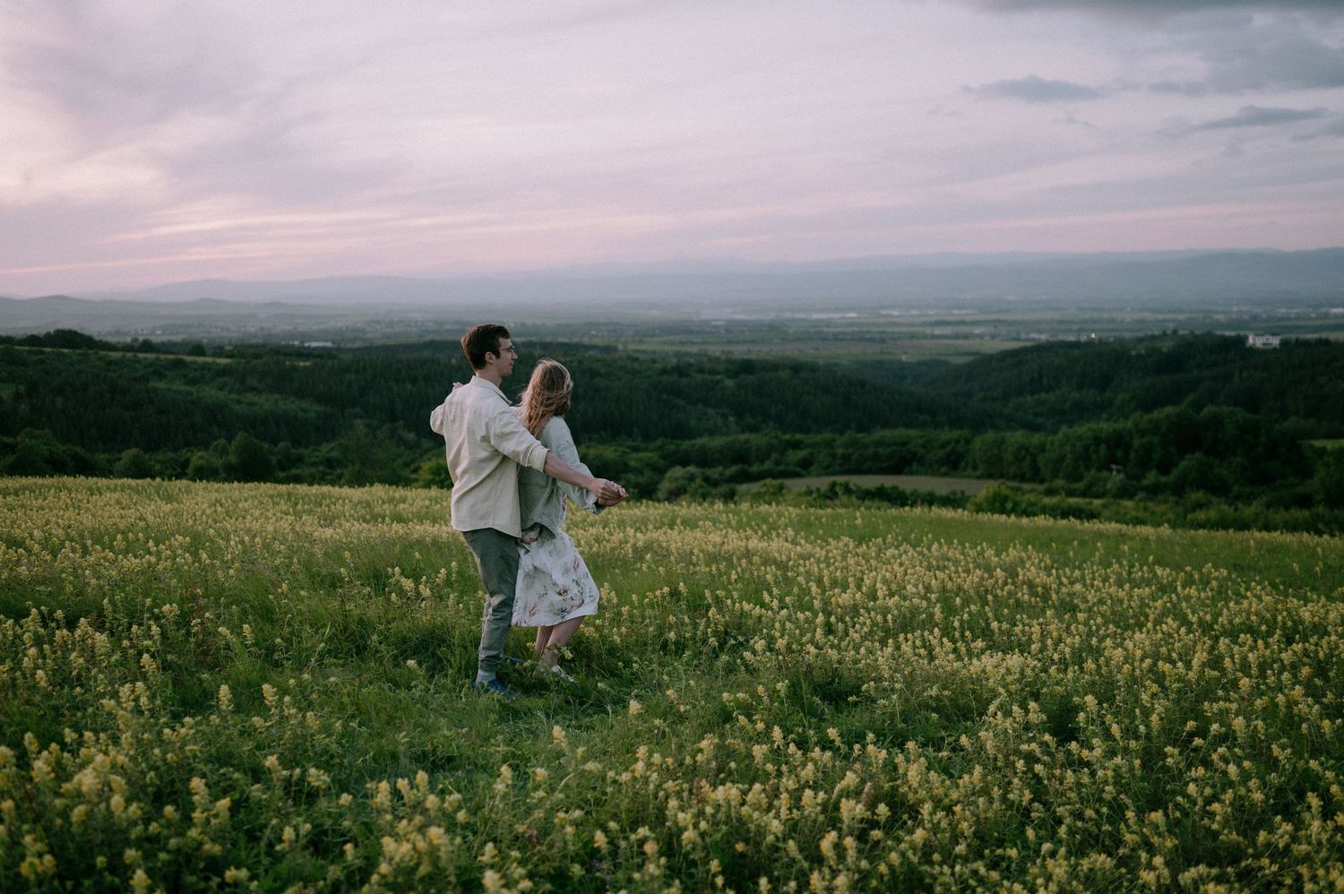 Couple sharing a tender moment in a wildflower field as the sun sets over distant hills.