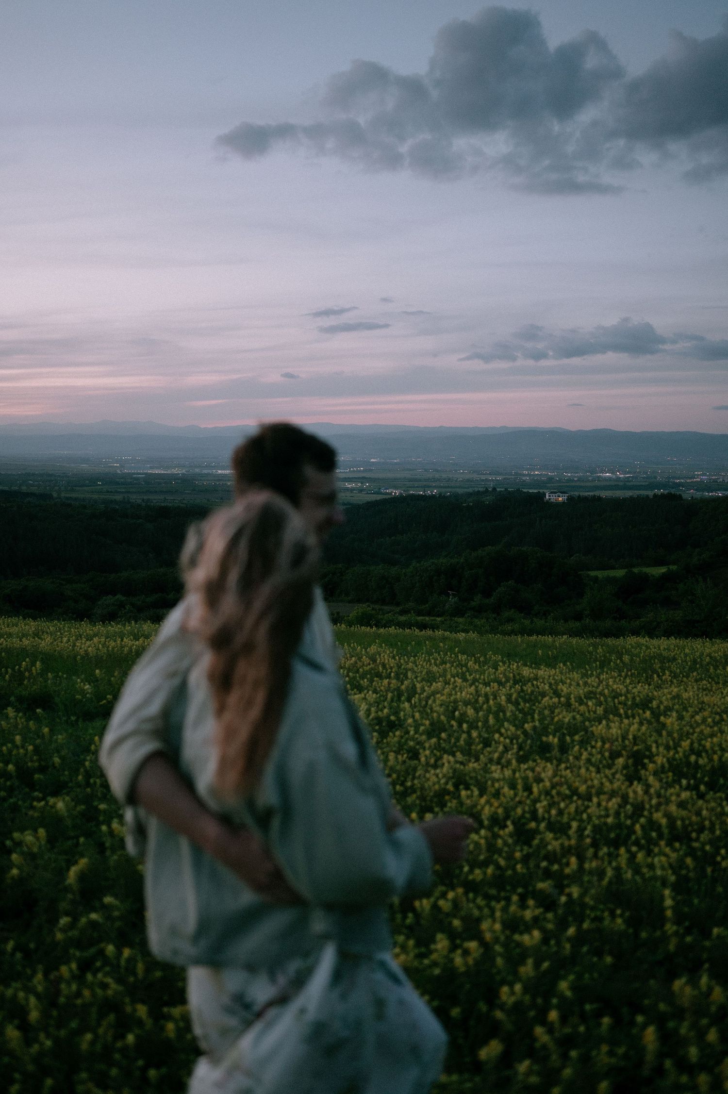 Moody sunset scene of a couple embracing in a hilltop flower field with dramatic clouds.