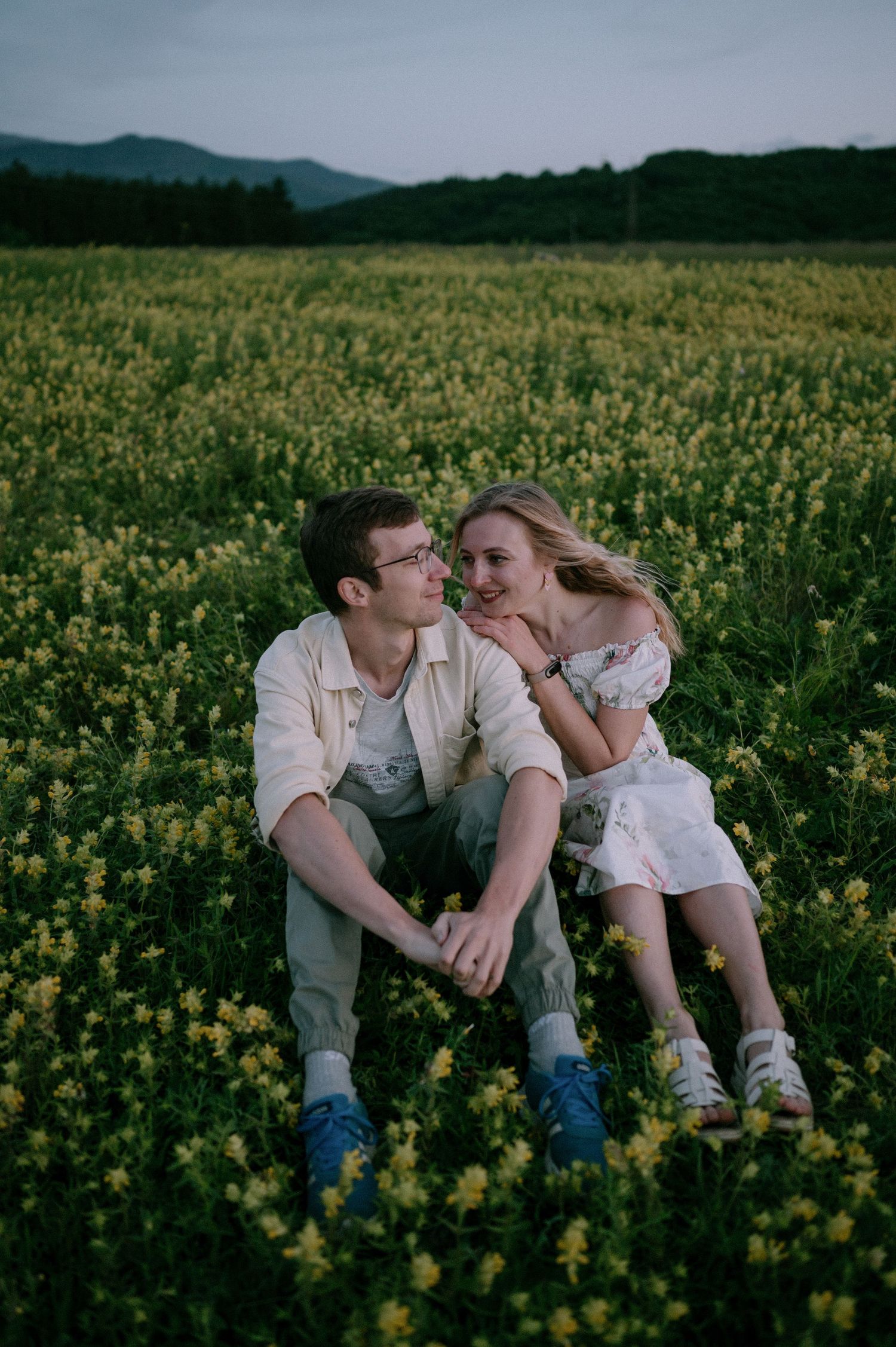 A couple relaxes together among yellow wildflowers in a scenic mountain valley.