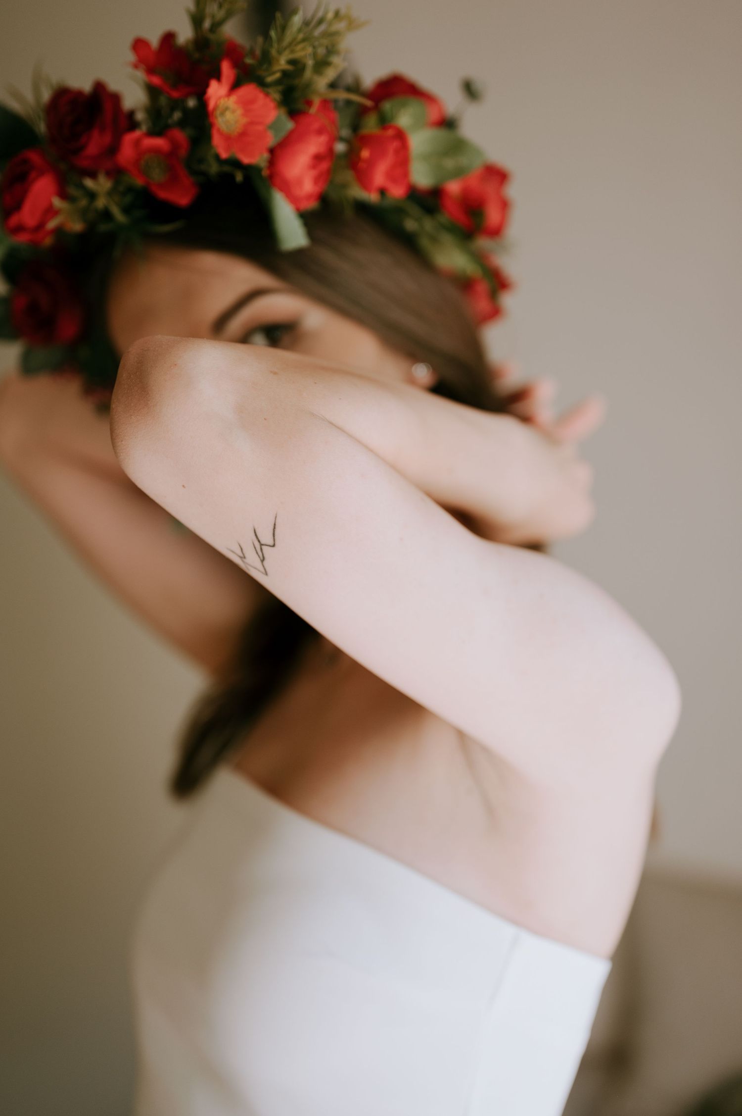 Artistic side pose showing delicate arm tattoo and red floral crown.