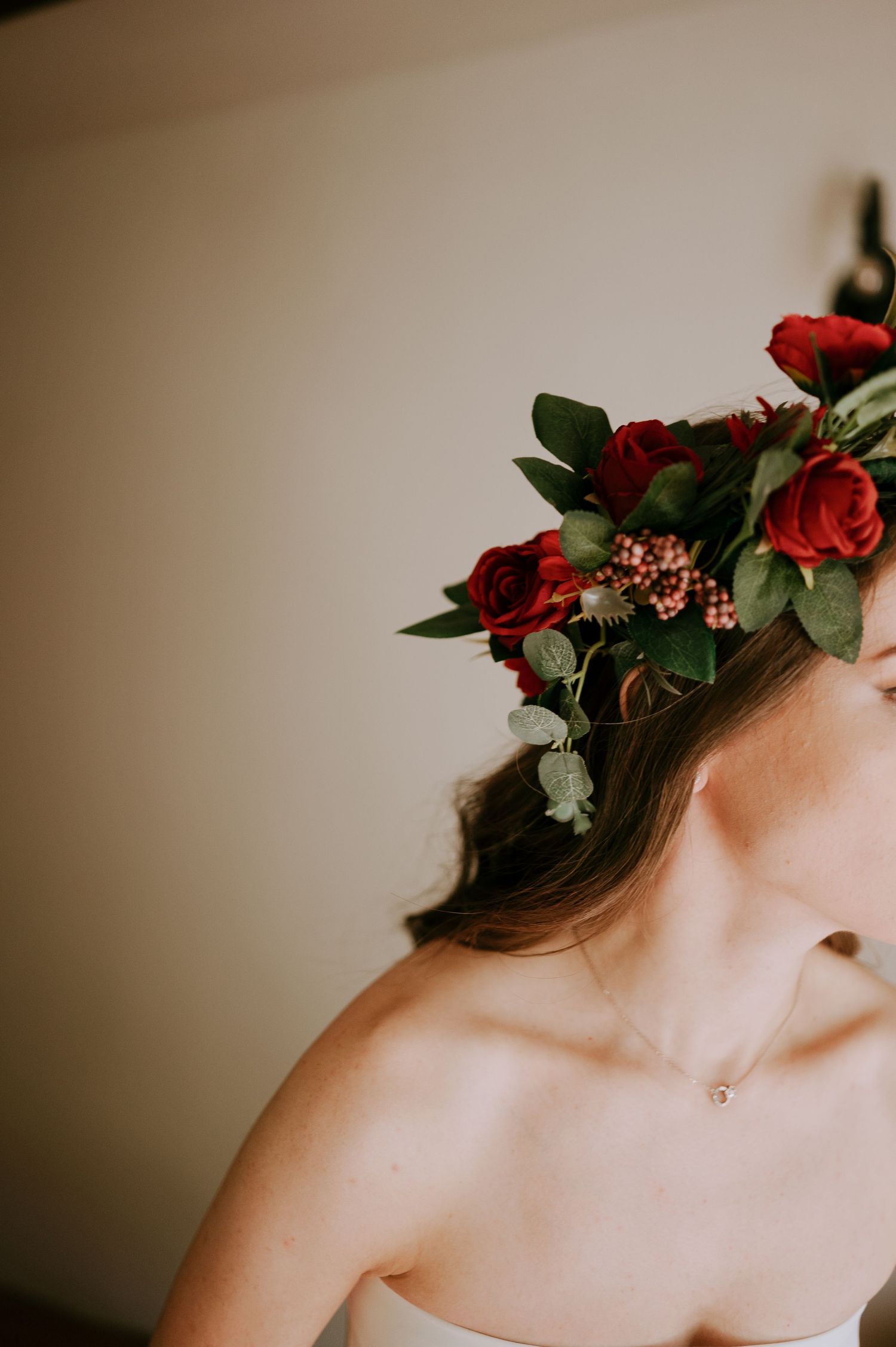 A delicate floral crown with red roses and greenery adorns a white wedding dress.
