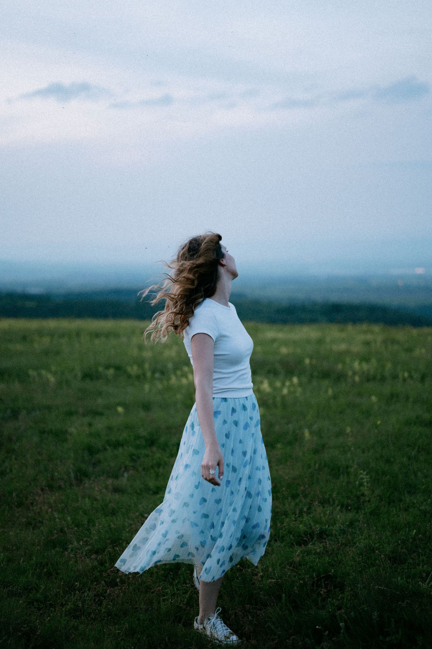 A person in white spins on a grassy hilltop with hair flowing in the wind.