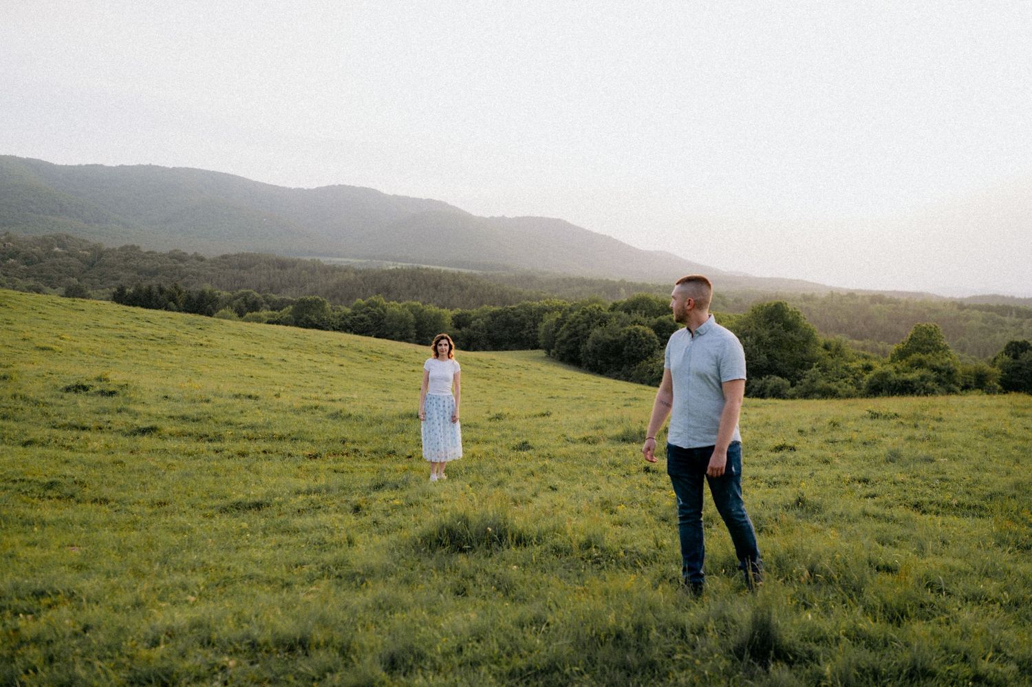 Two people walking together across a vast green hillside landscape.