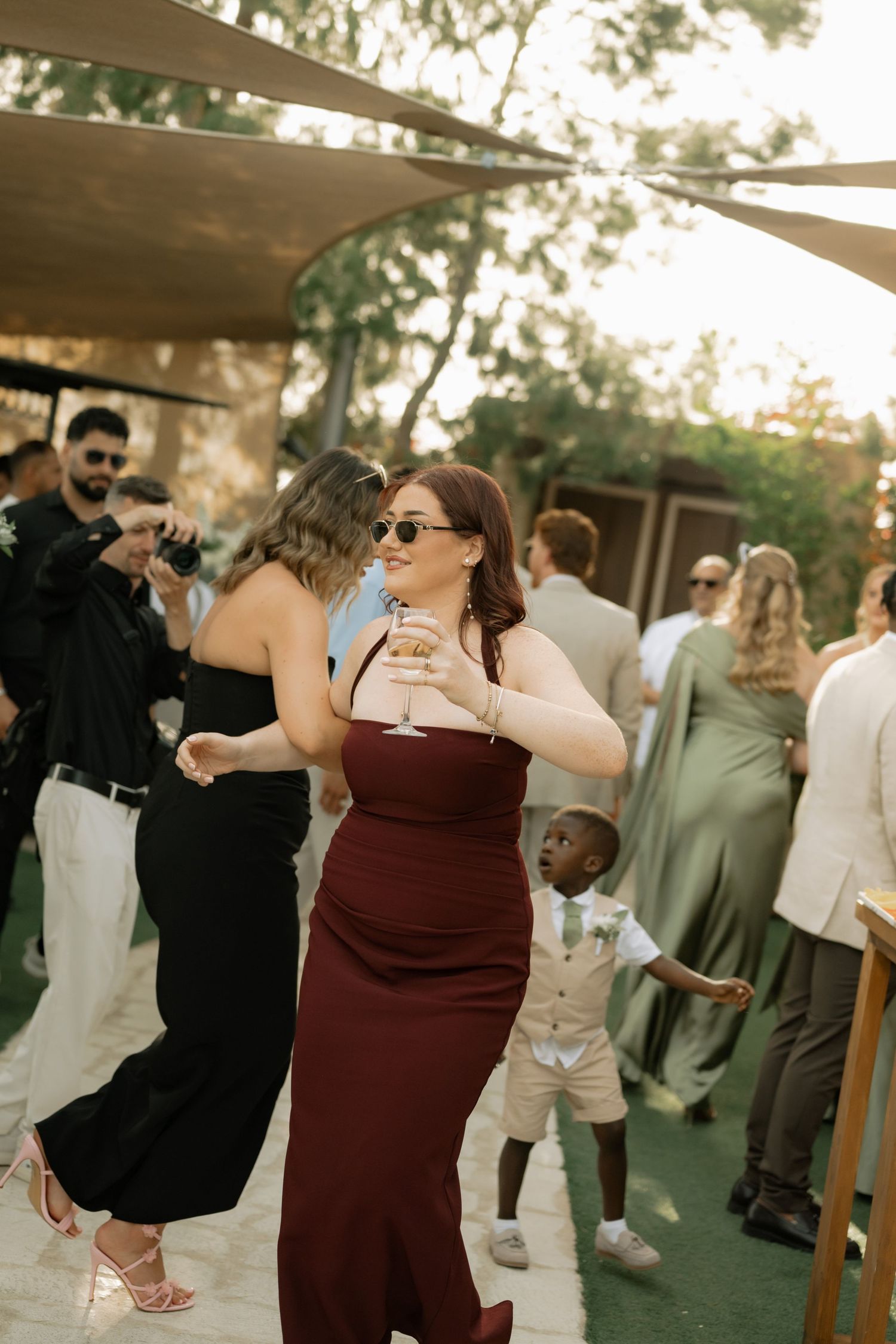 Guests dancing outdoors at a wedding reception, woman in burgundy dress holding a cocktail glass.