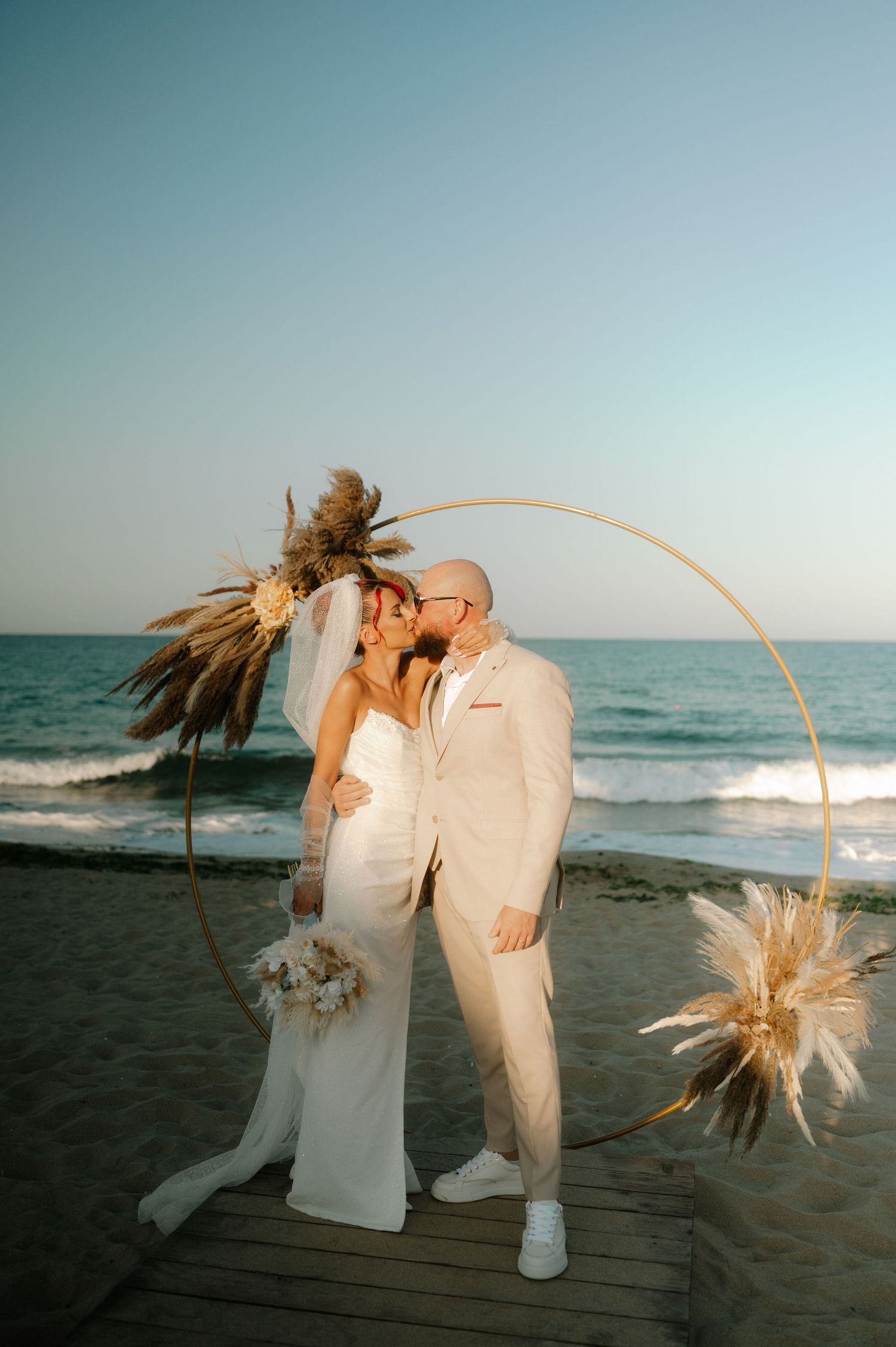 Intimate wedding portrait on a beach boardwalk with an elegant circular arch decorated with dried florals.