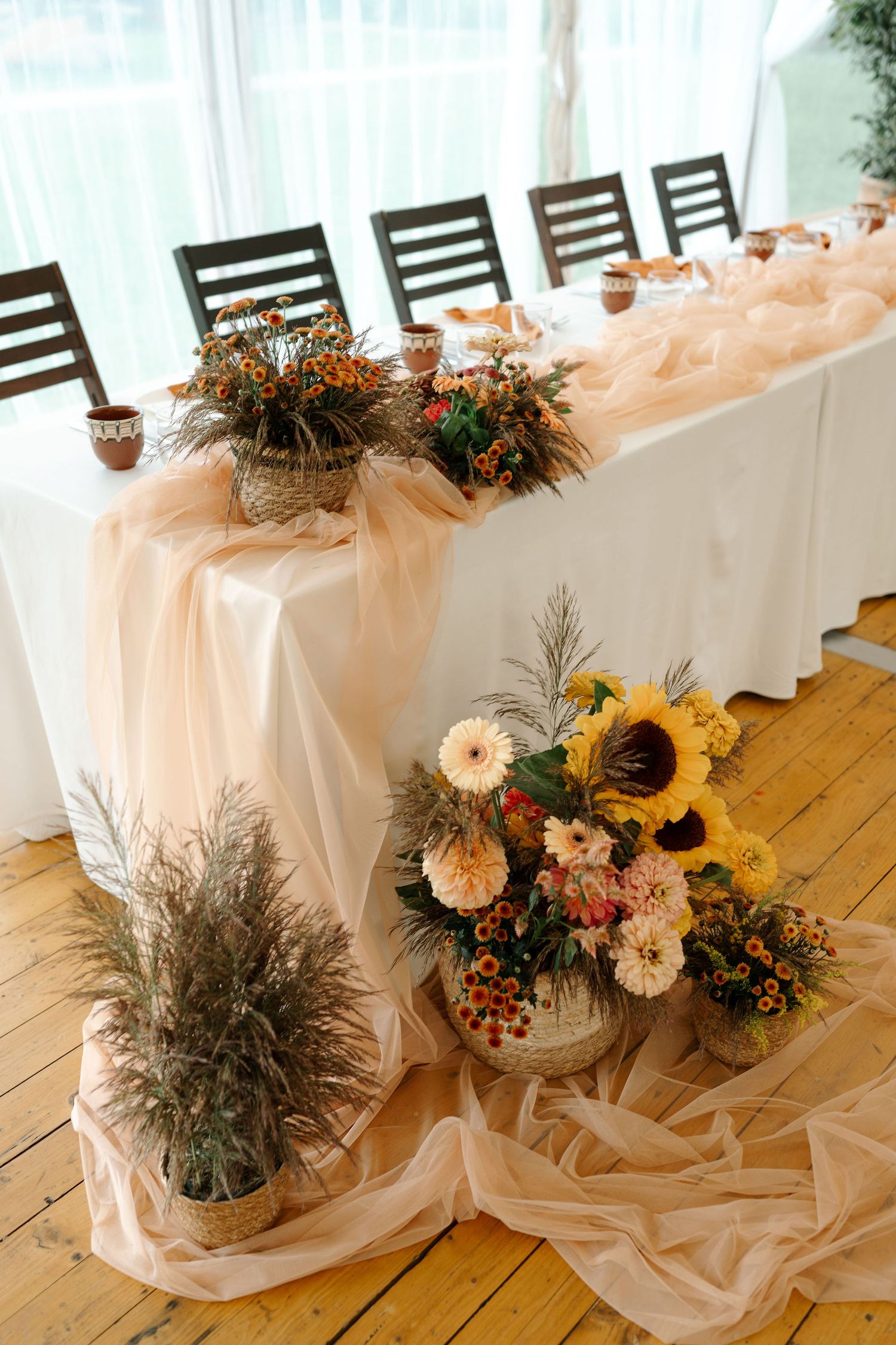 Elegant wedding reception table settings with sunflowers and floral arrangements on white tablecloths and wooden chairs.