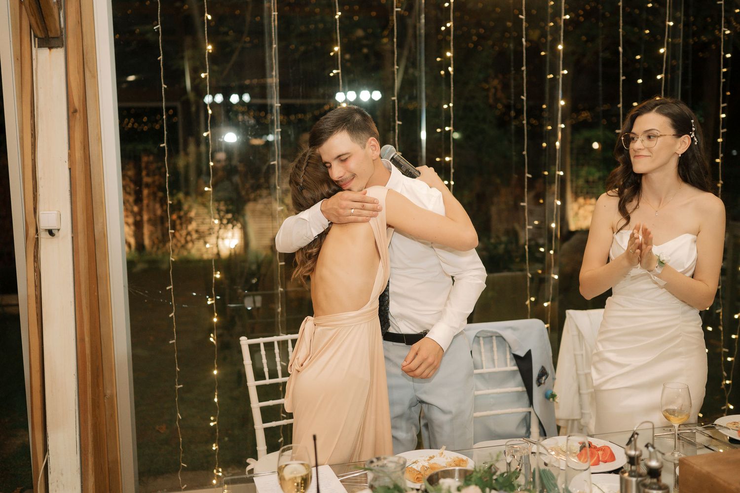 Wedding guests enjoying a romantic evening reception under twinkling string lights in an elegant indoor venue.