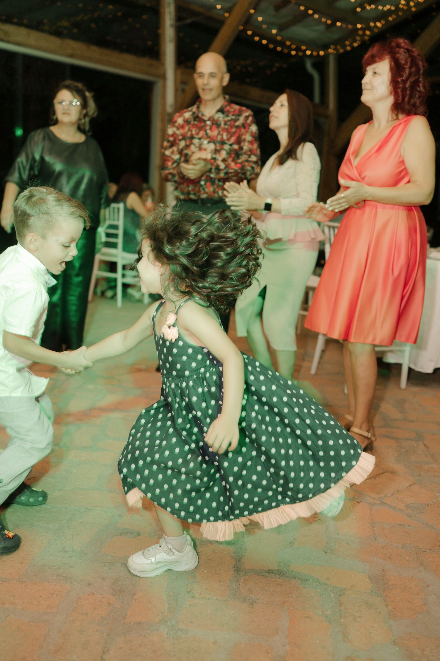 People dancing at an evening event with string lights overhead, featuring a green polka dot dress on the dance floor.