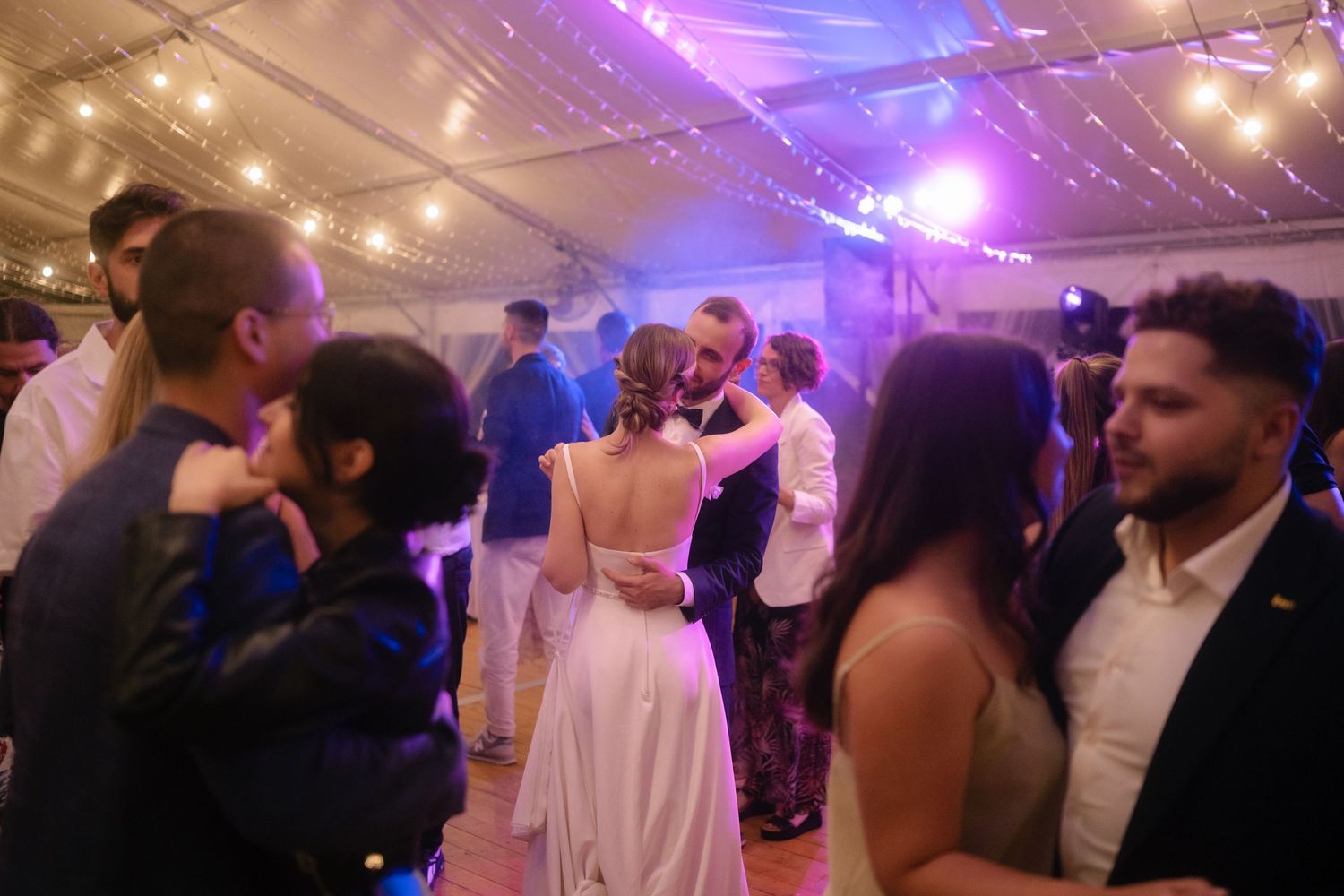 Wedding reception dance floor illuminated by purple uplighting and warm string lights creating a festive atmosphere.