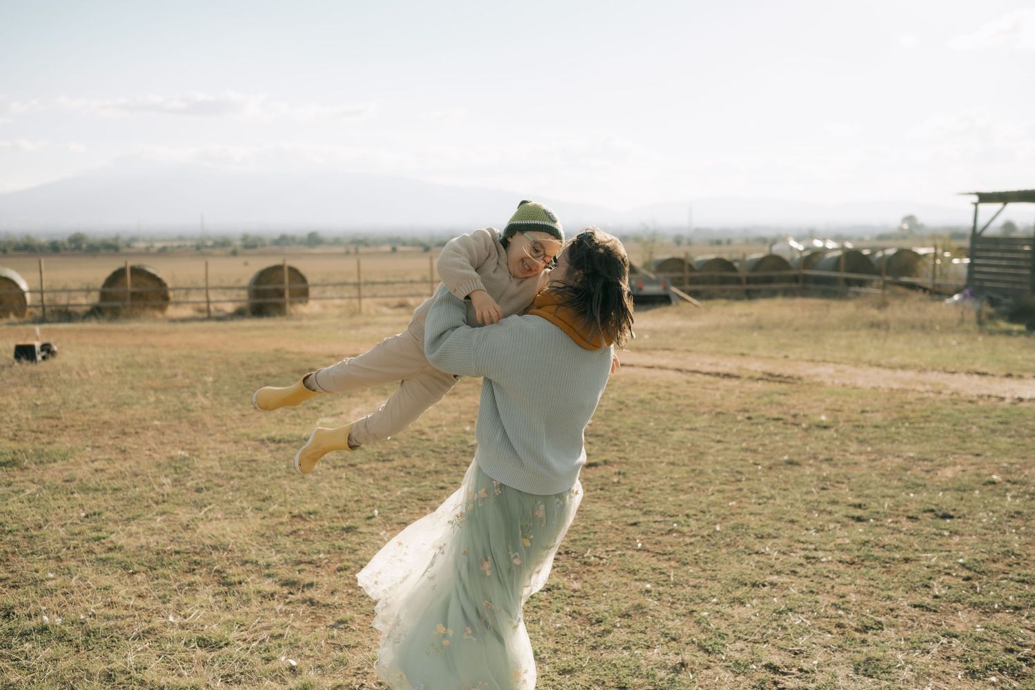 A couple in a rural field embrace in a romantic dance pose with mountains visible in the background.