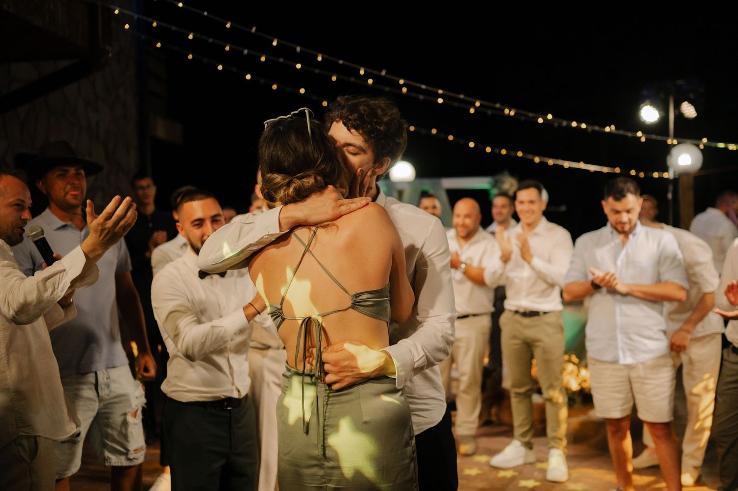 Wedding reception dance party under string lights with guests in white attire celebrating on the dance floor.