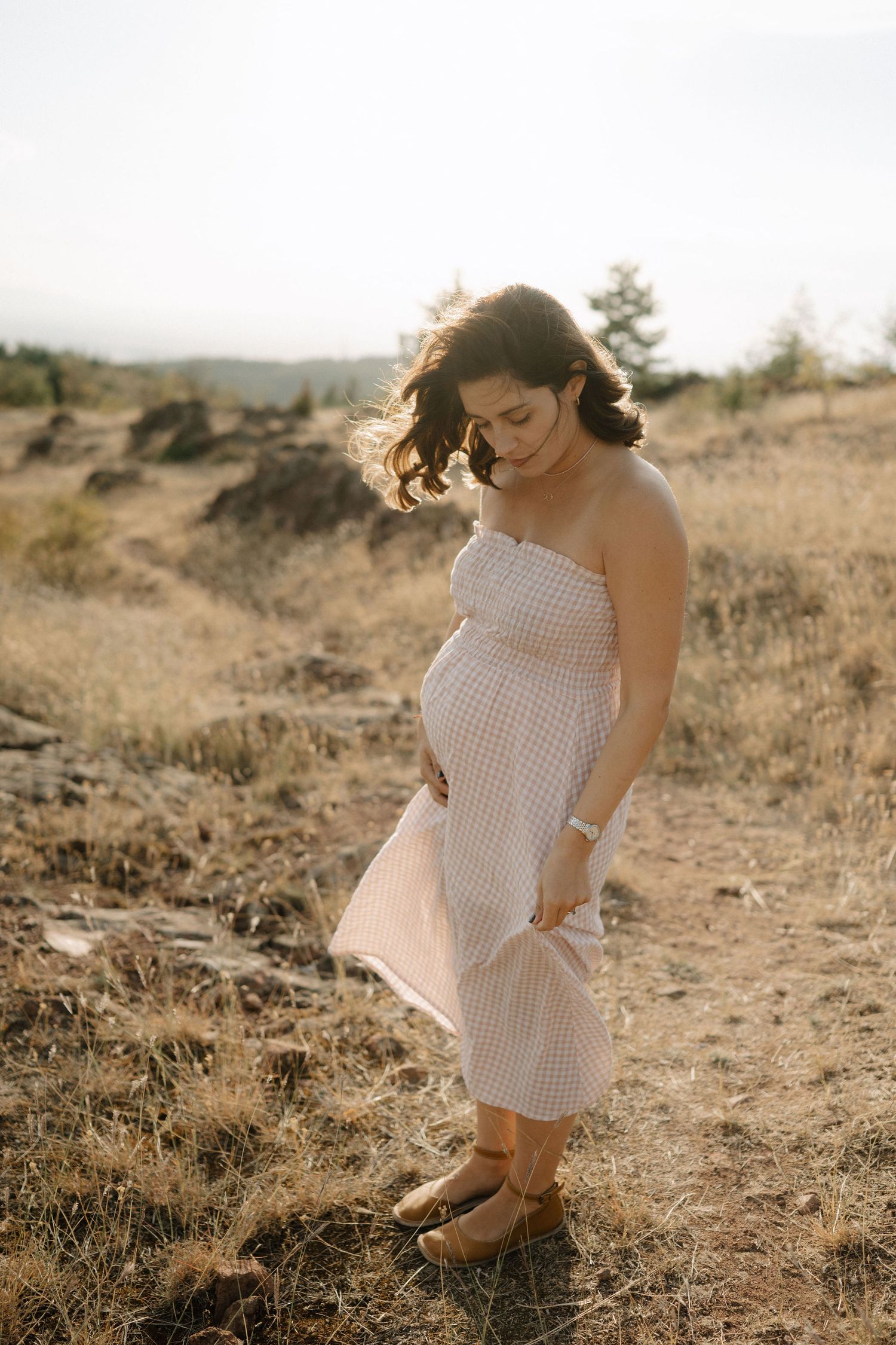 A person in a white polka dot dress sits gracefully in a golden field during sunset.