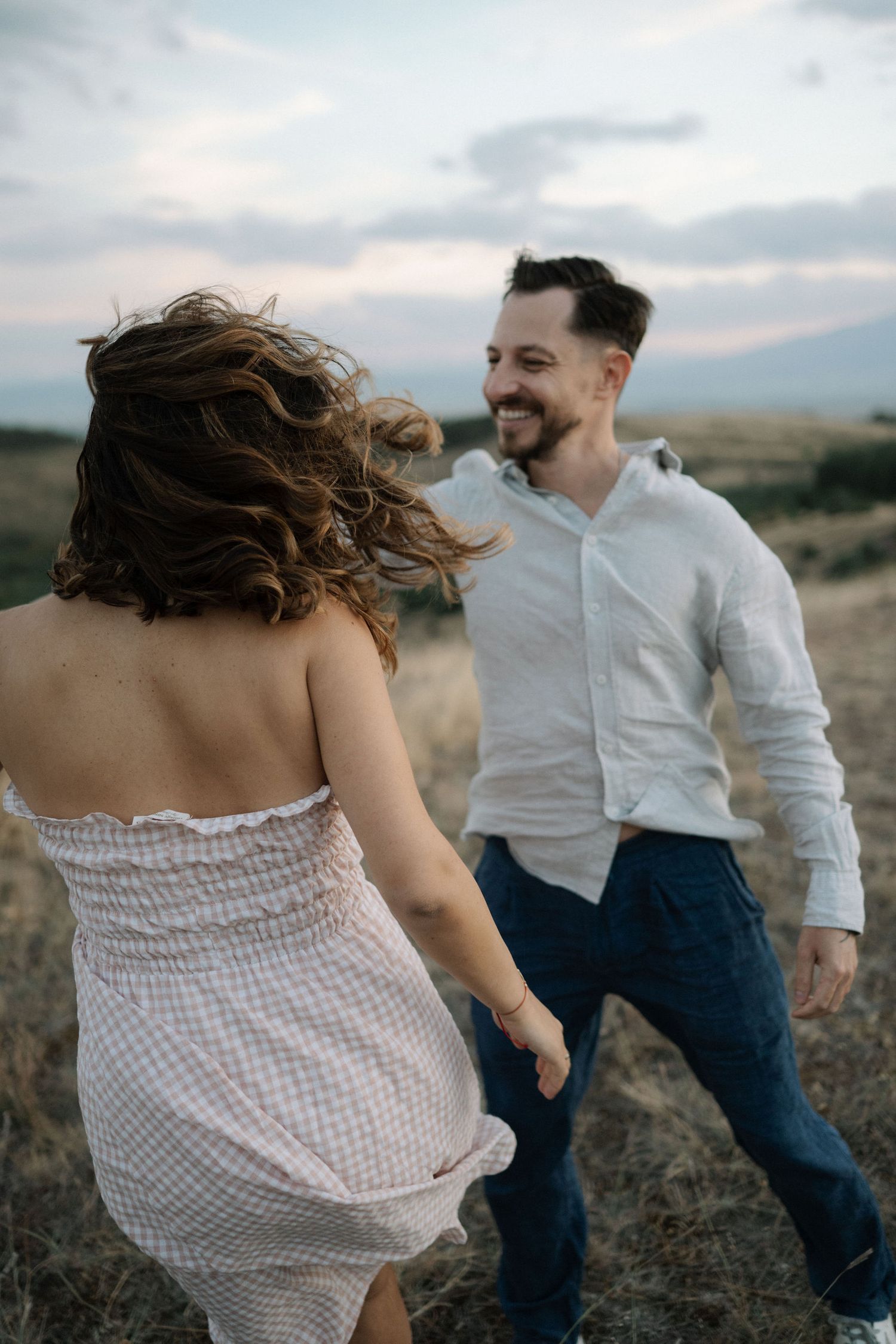 A couple dances and laughs together in a rustic outdoor setting during golden hour.