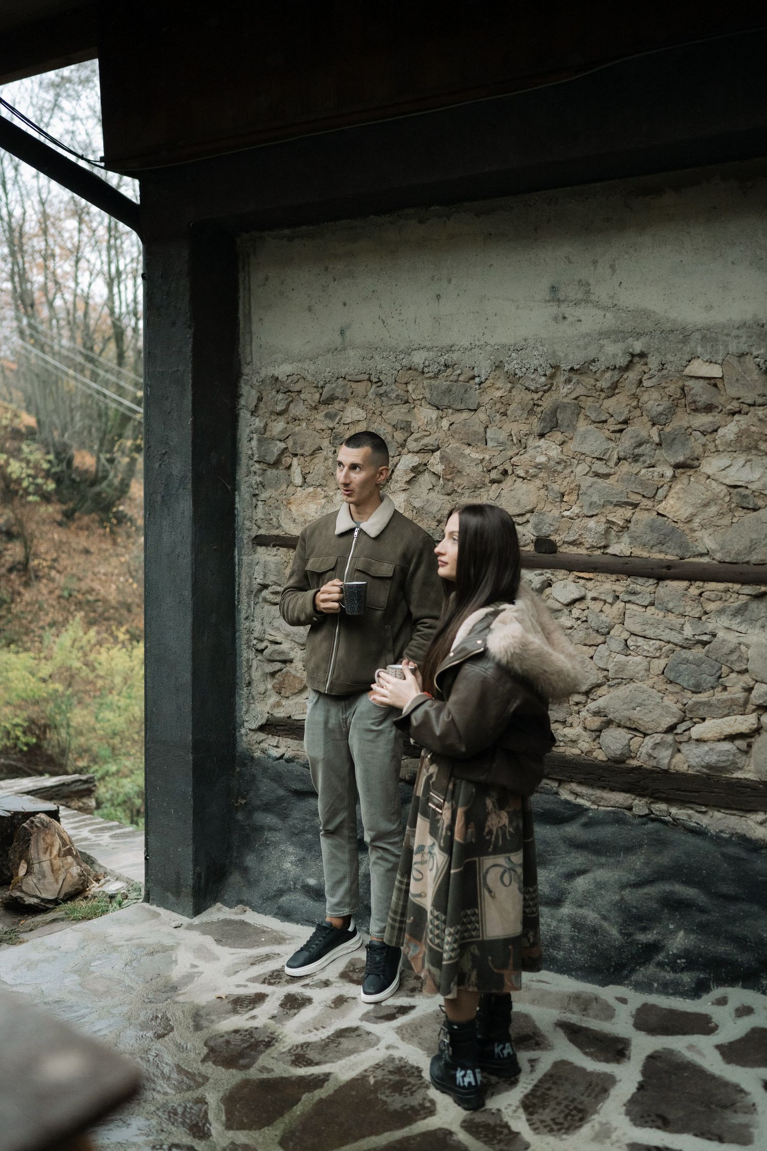 A couple shares a romantic moment in front of a rustic stone wall during an outdoor photoshoot.