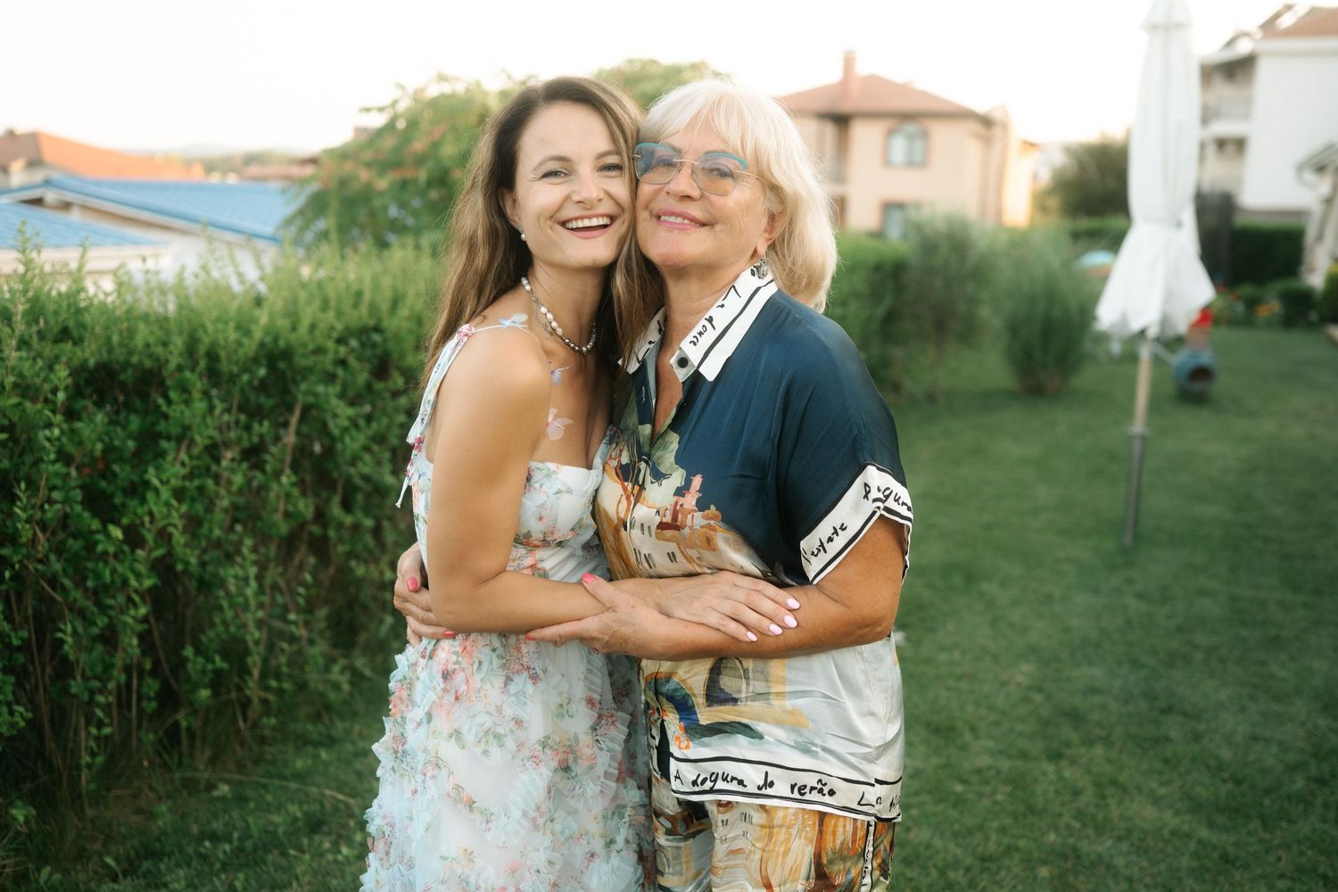 Two people share a joyful embrace while standing together on a grassy lawn during a sunny outdoor gathering.