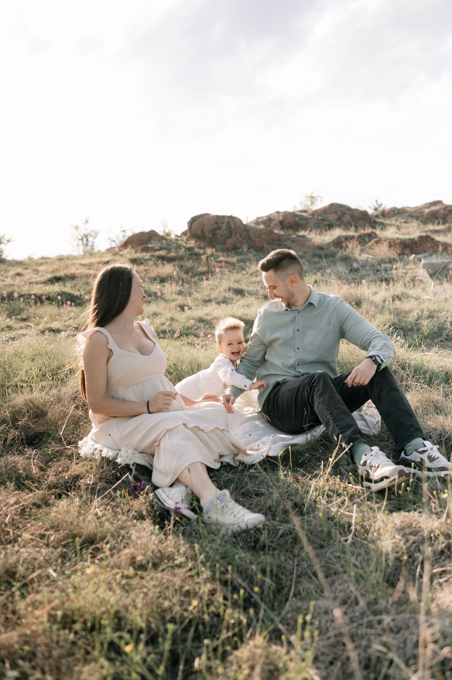 A family sits together on a grassy hillside during golden hour, enjoying a peaceful outdoor moment together.
