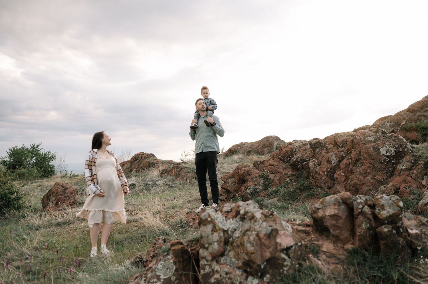 Two people stand among rocky terrain on a cloudy day with one person elevated on rocks while another watches from below.