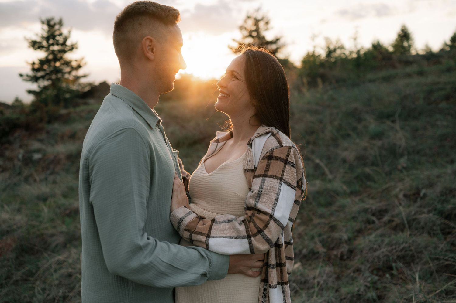 Couple sharing romantic sunset moment in rustic outdoor setting with mountains and evergreen trees in background.