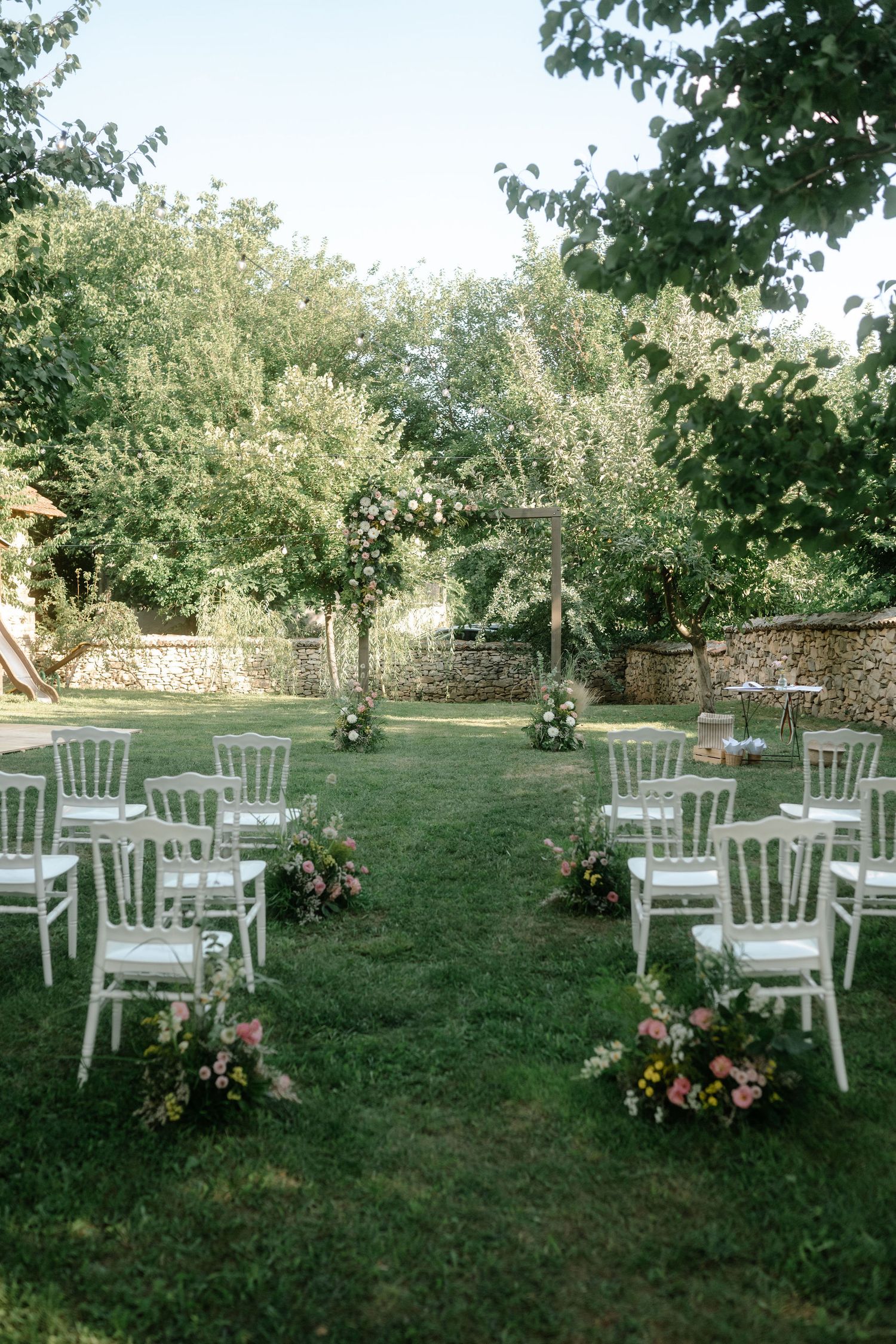White wooden chairs arranged in rows on a grassy lawn for an outdoor garden ceremony or event.