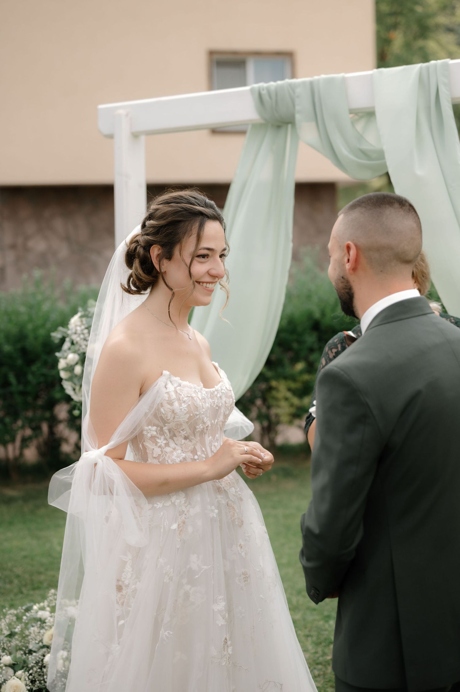 A tender first look moment between a bride in a floral lace gown and groom in a dark suit during their wedding day.
