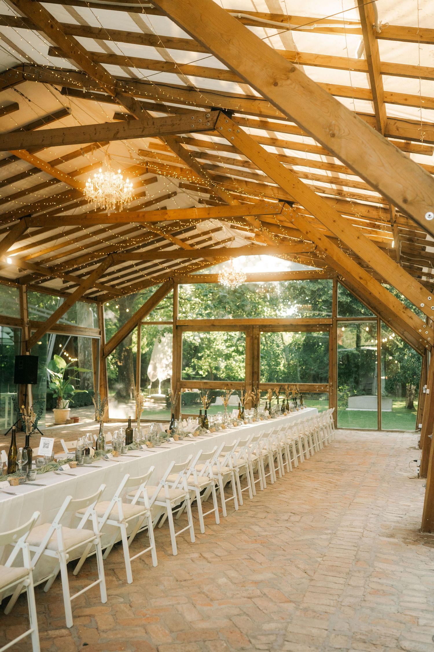 Long rustic wooden pavilion with exposed beams and rows of white folding chairs set up for an outdoor wedding ceremony.