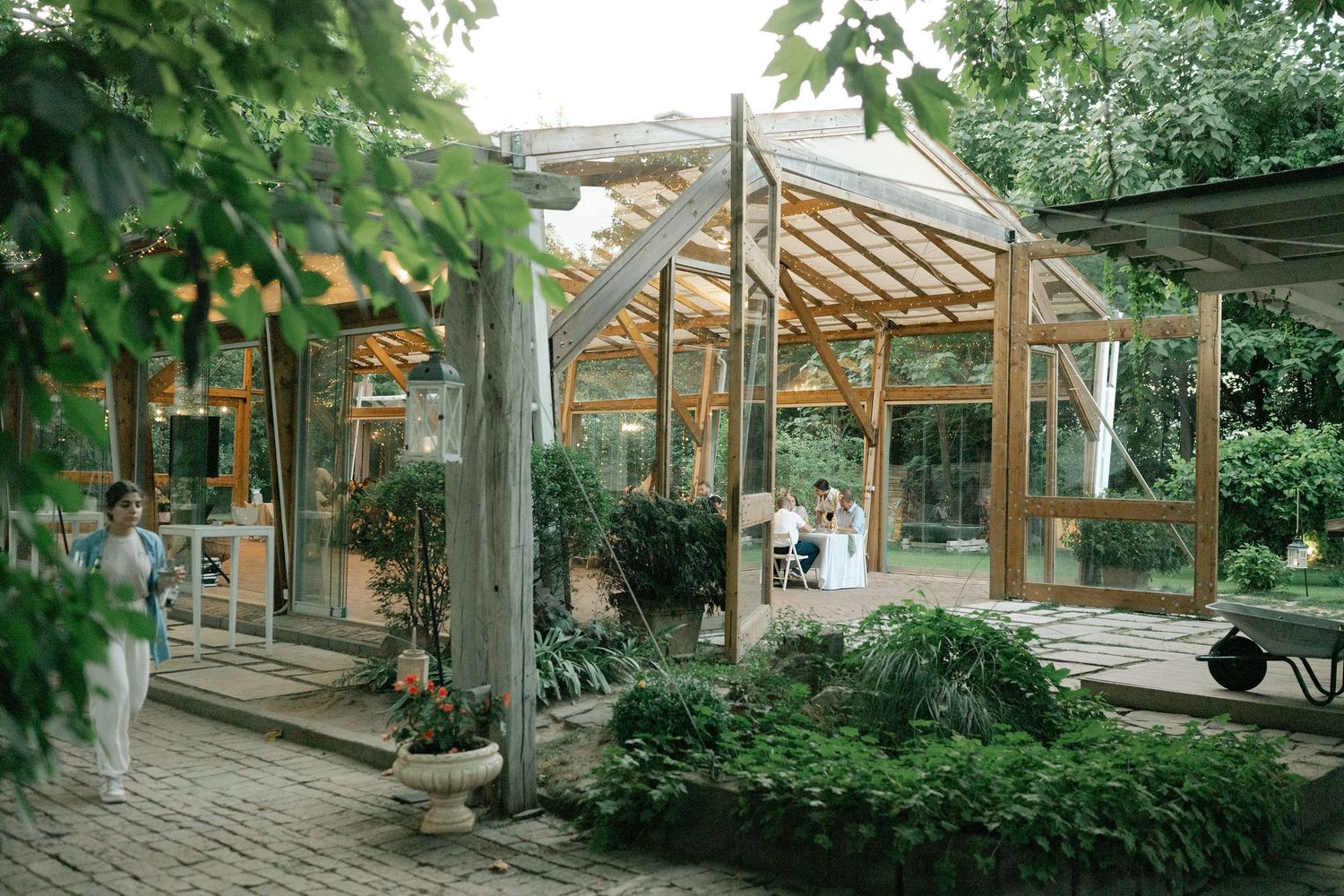 A series of connected greenhouse structures with wooden beams and glass panels surrounded by lush greenery and plants.